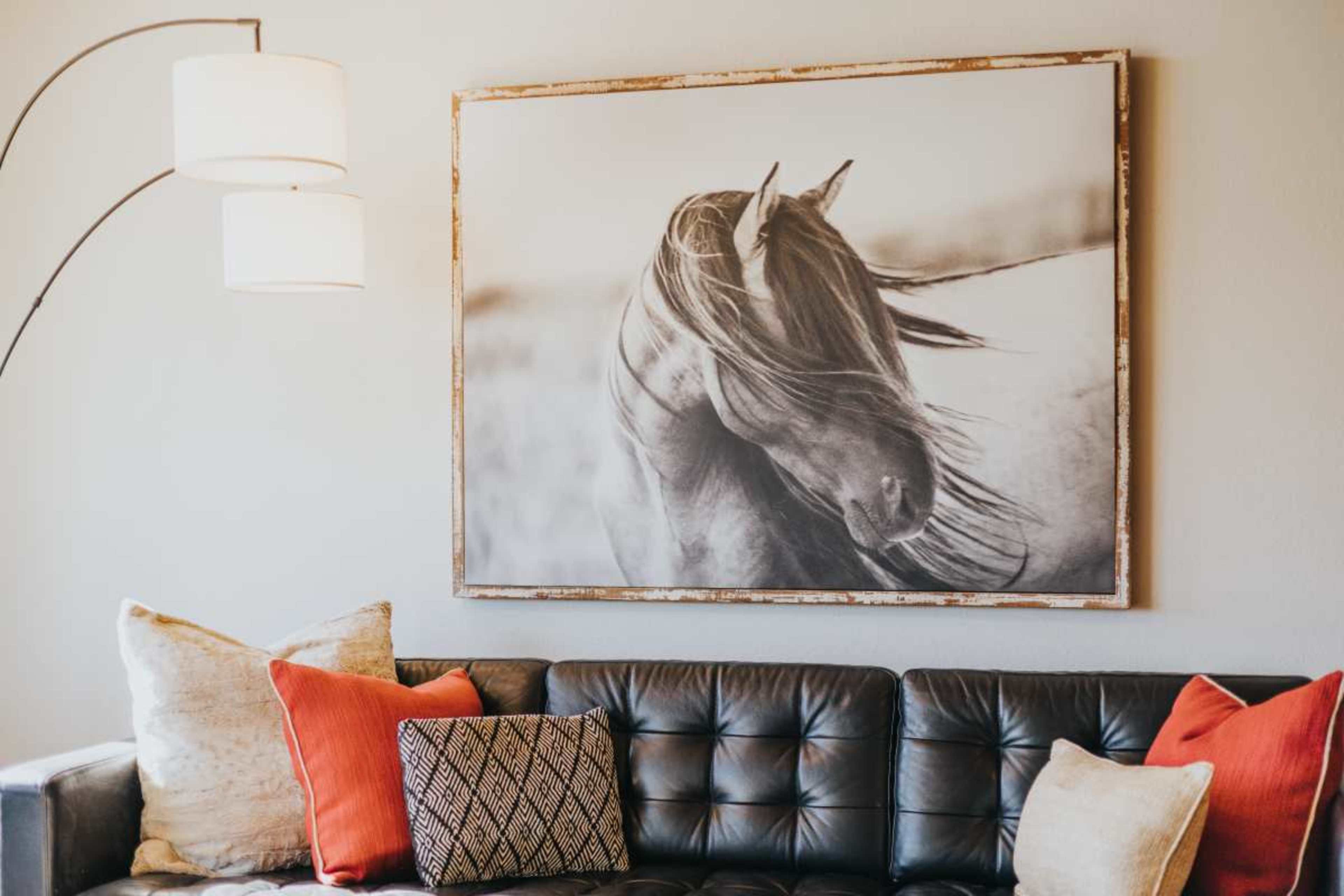 A black leather couch with decorative pillows is positioned against a wall featuring a large black-and-white photograph of a horse.