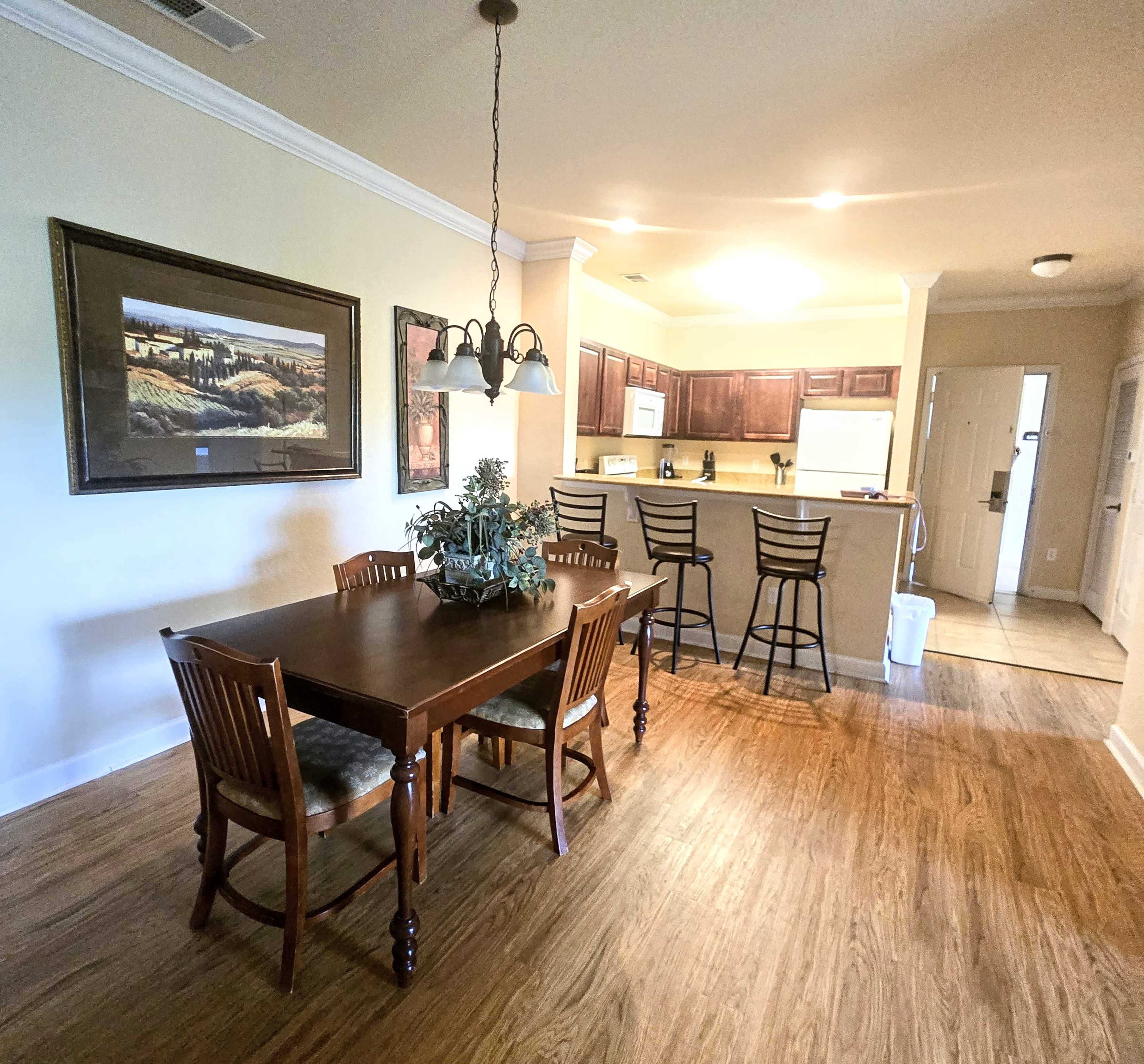 A dining area with a wooden table and chairs, leading into a kitchen with bar seating and dark cabinetry.