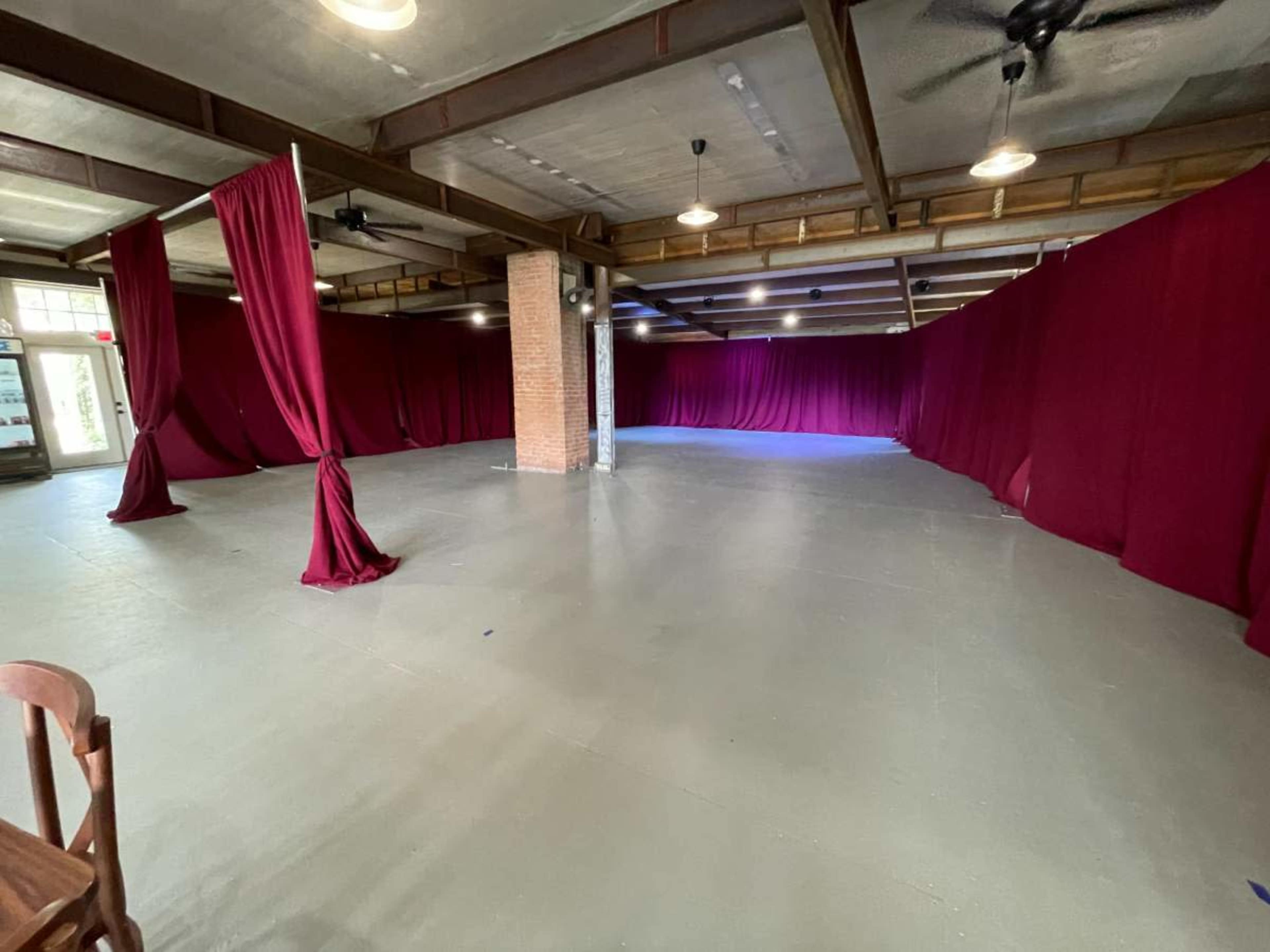 The room features an empty, spacious area with maroon curtains draping along the walls and a polished concrete floor.