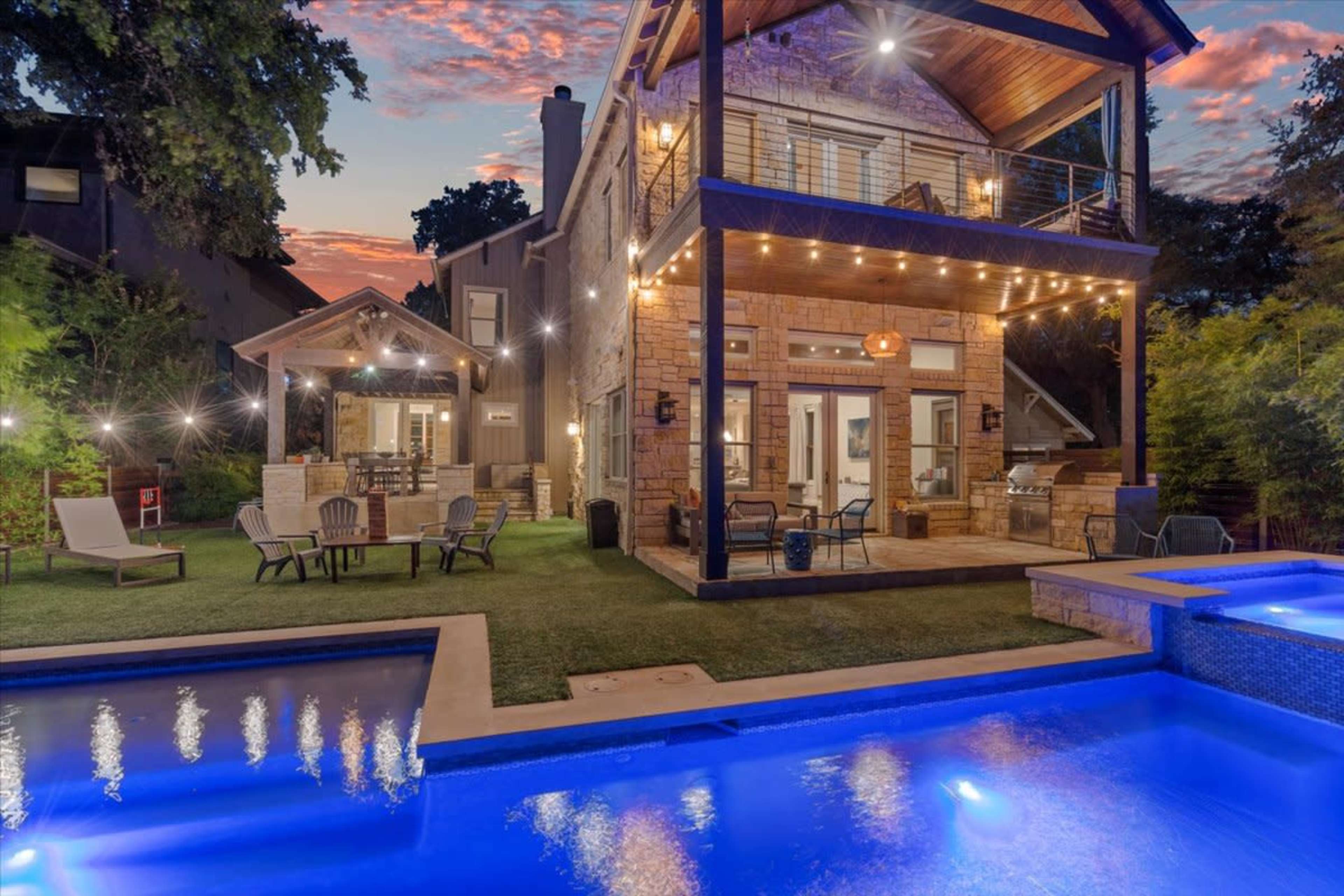 A two-story house with a patio and a swimming pool, illuminated by string lights during sunset.