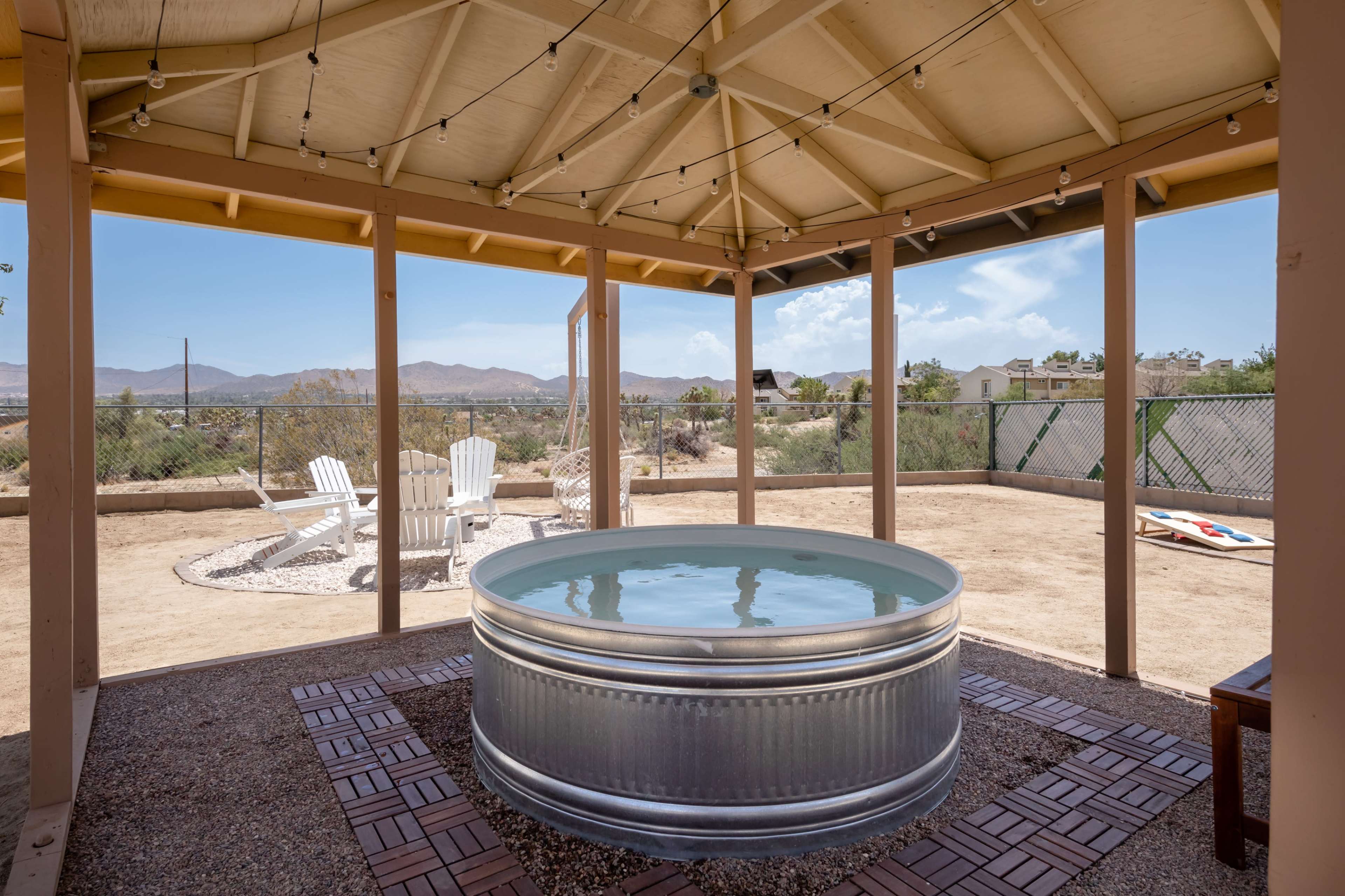 The image features a circular metal above-ground pool situated under a wooden gazebo with a panoramic view of a desert landscape.