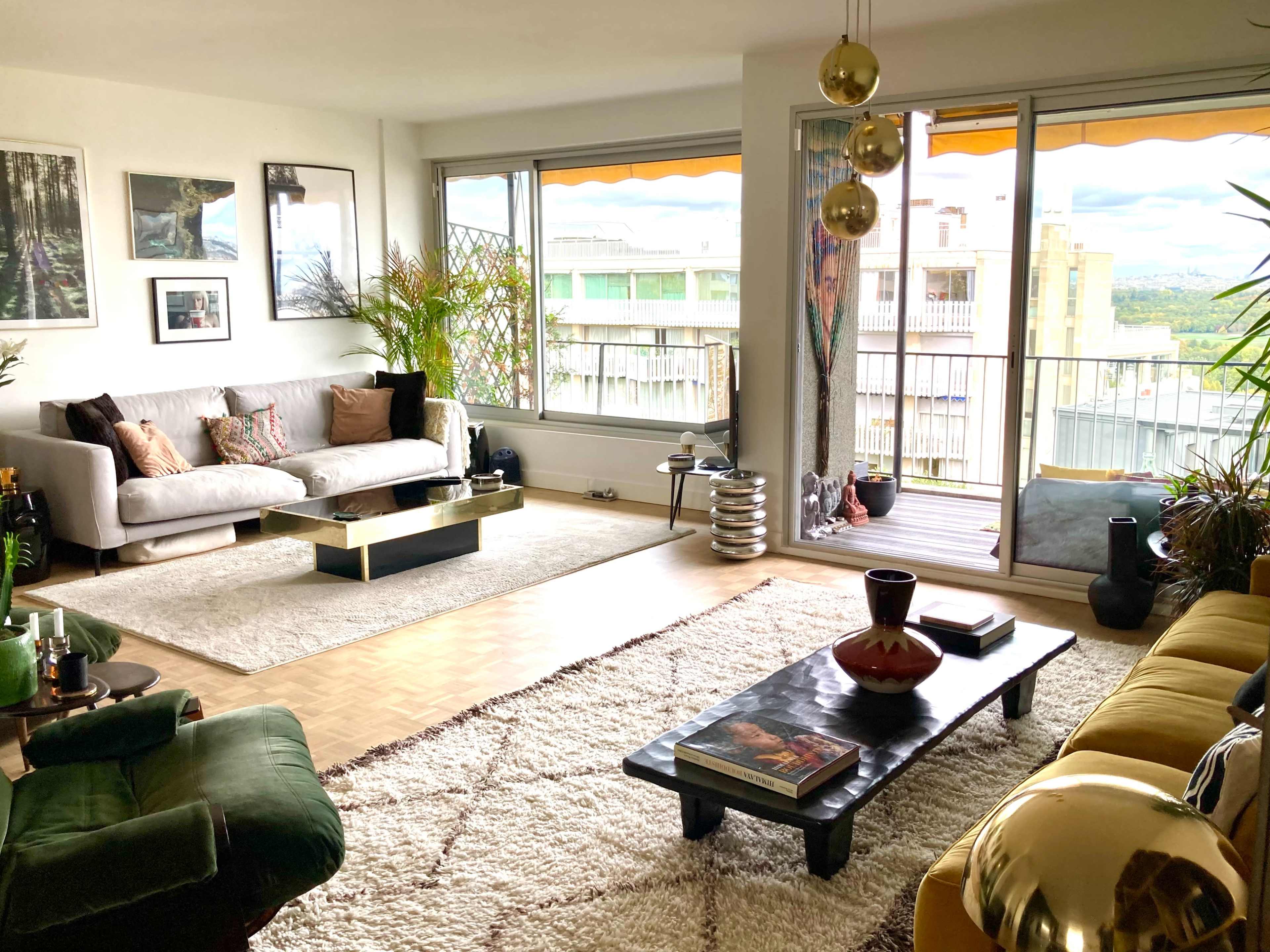 A modern living room features two sofas, a coffee table, and large windows overlooking a balcony with a scenic view.