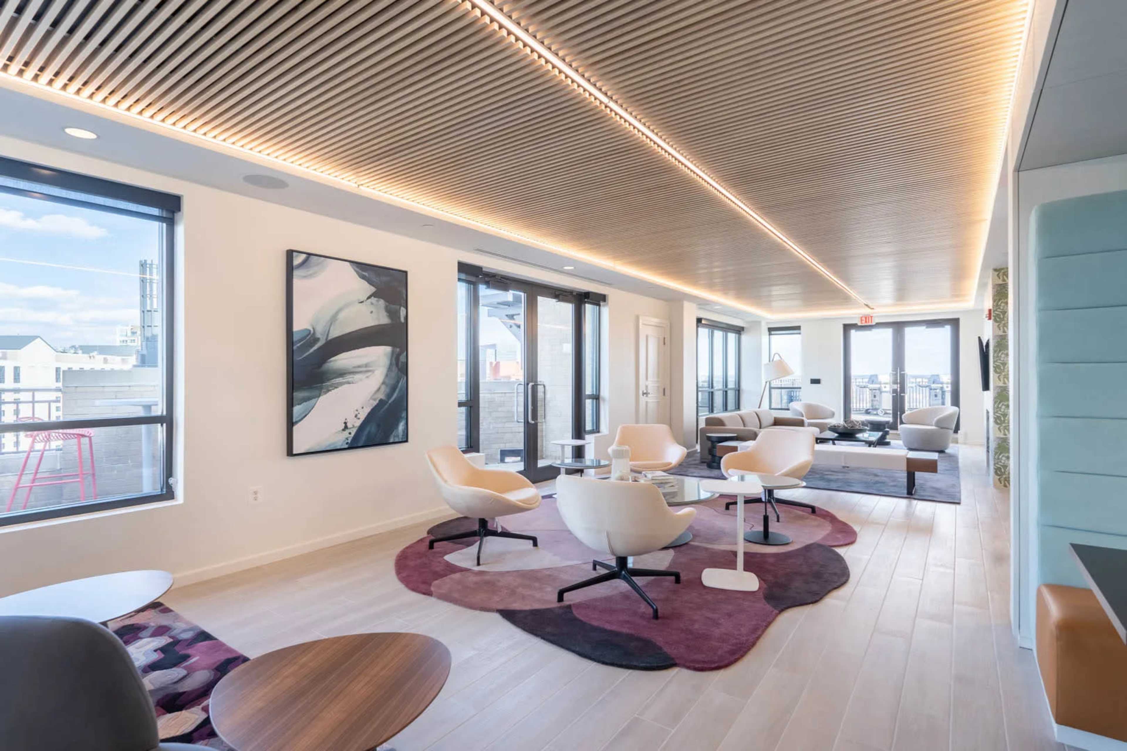 A modern lounge area with large windows, contemporary furniture, and a wooden ceiling.