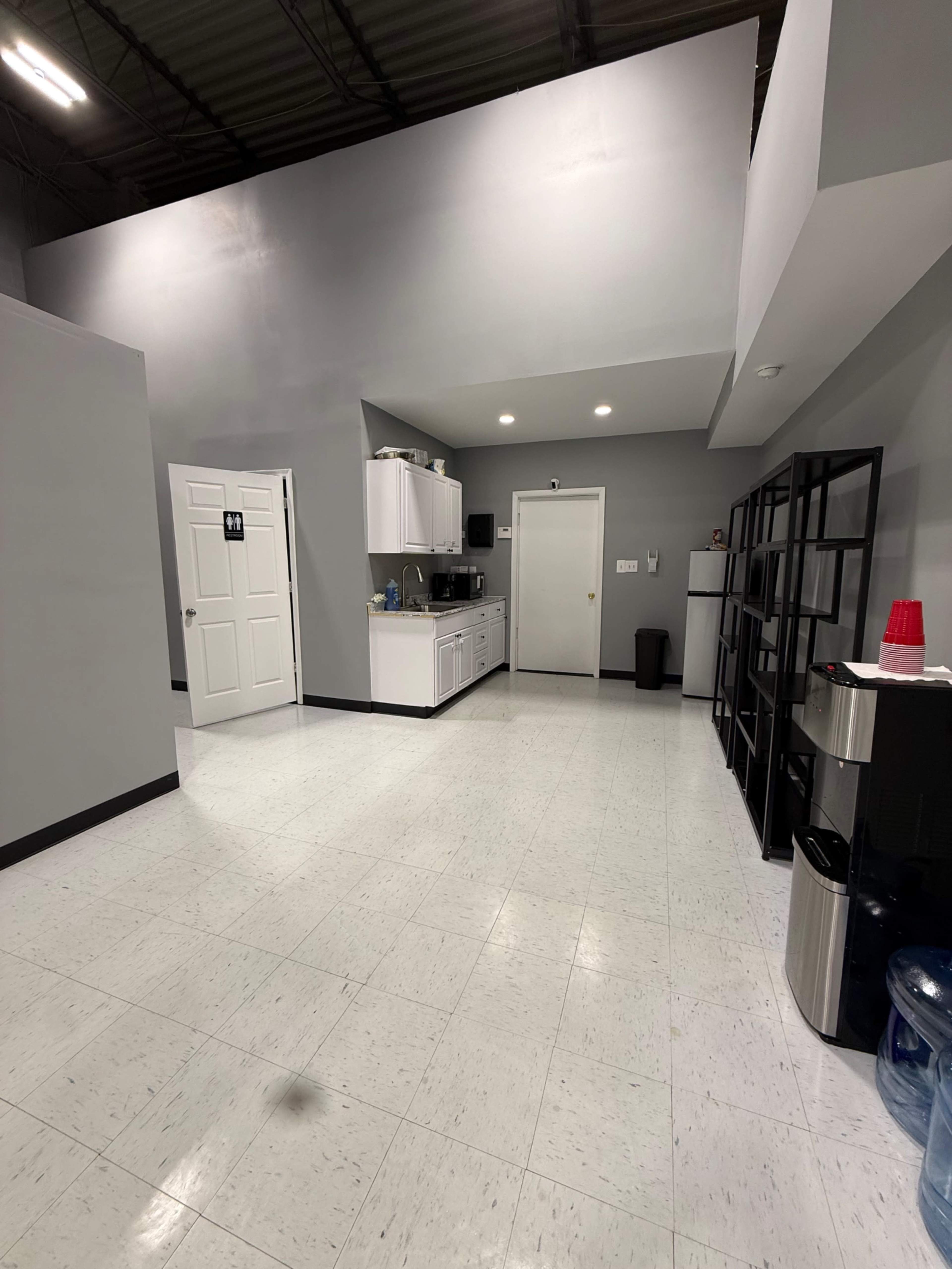 The image shows a spacious, gray-walled break room with a kitchenette, a restroom door, and large cabinets.