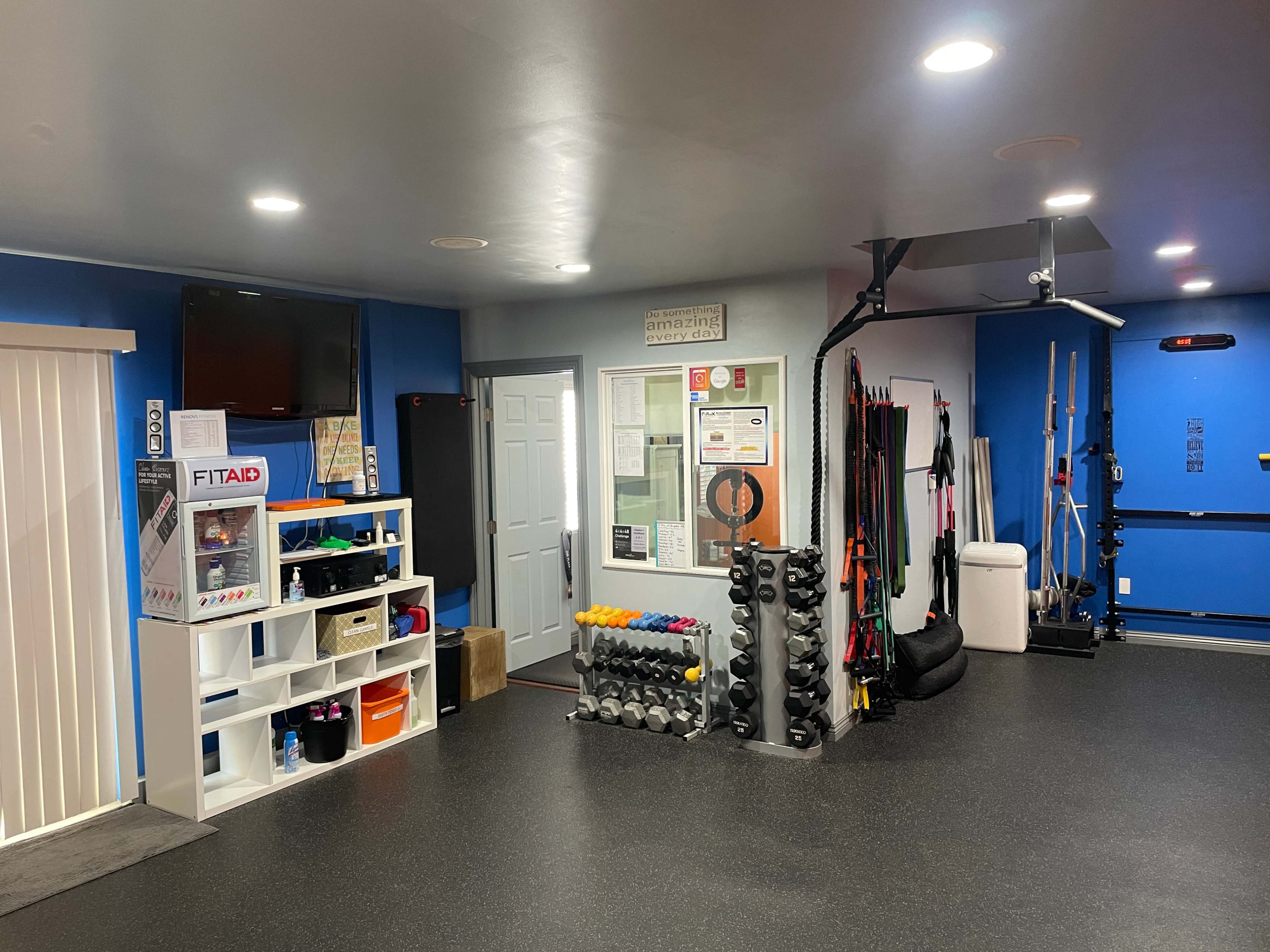 A well-organized home gym featuring a variety of fitness equipment, a shelving unit with storage bins, and a wall-mounted television.