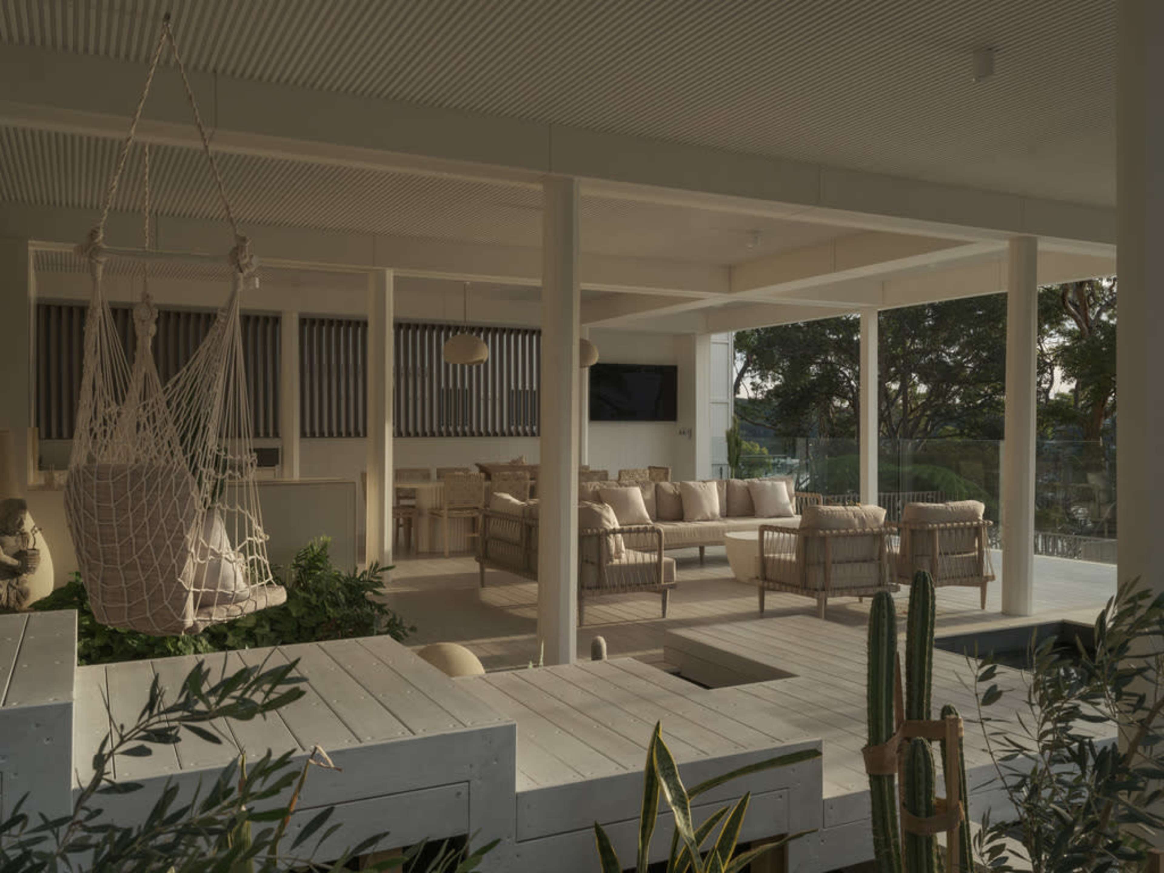 The image shows a modern, open-air living space with comfortable seating, a hanging chair, and greenery integrated into the design.
