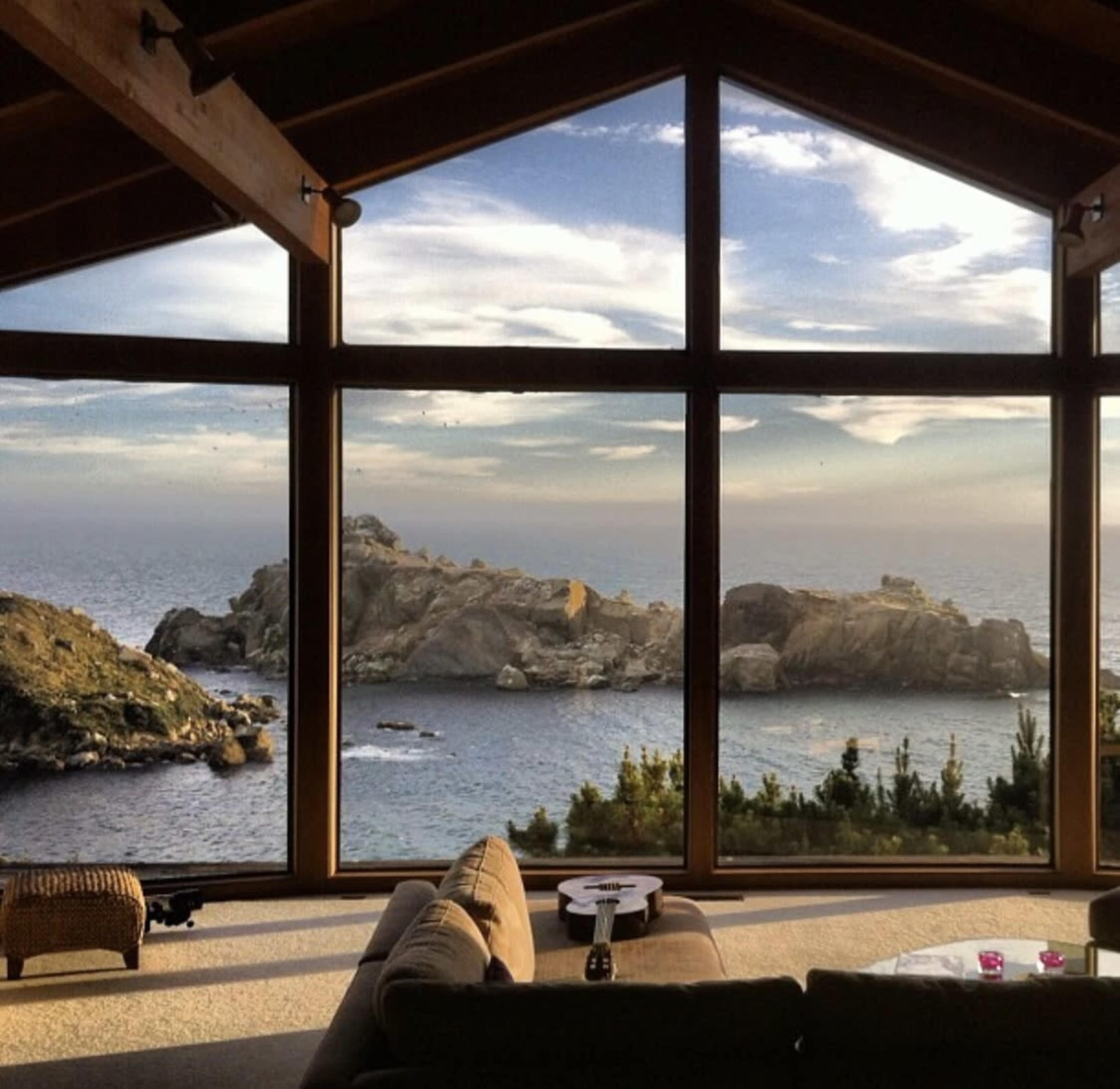 A spacious living room with large windows showcases a coastal view of rocky cliffs and the ocean.