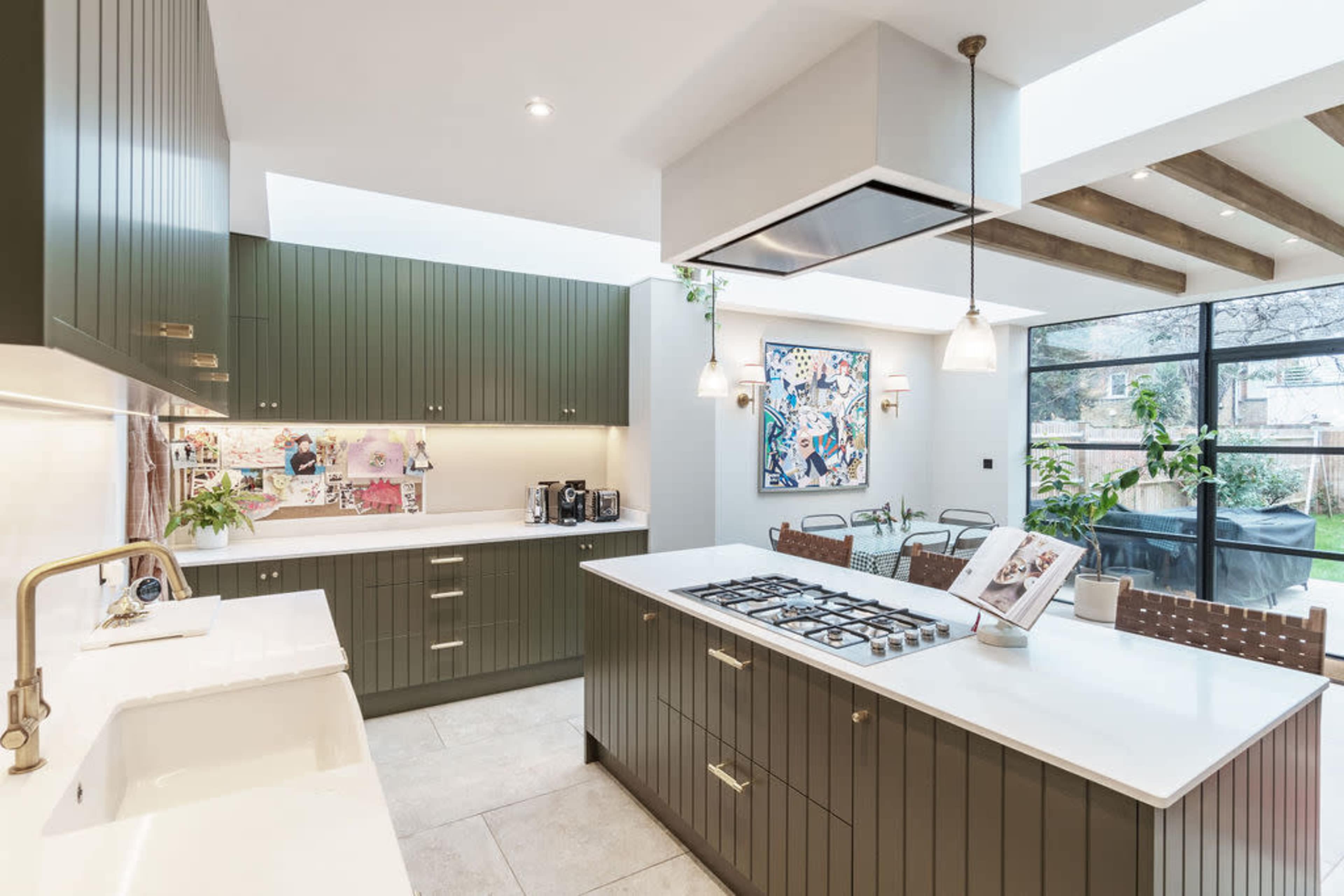The kitchen features green cabinetry, a large island with a gas stove, and a large window that allows natural light to fill the space.