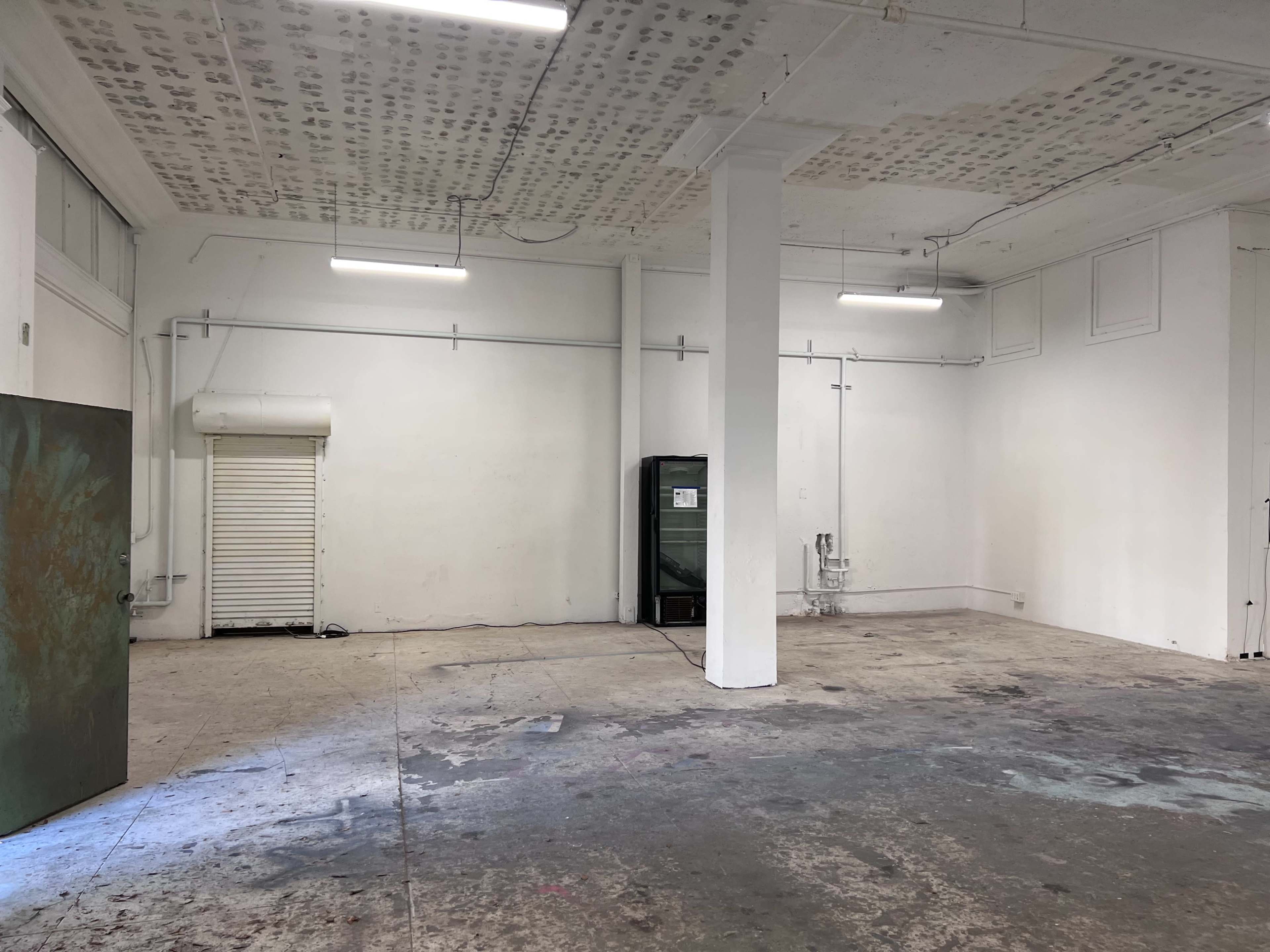 An empty room with bare walls, a concrete floor, and fluorescent lighting.