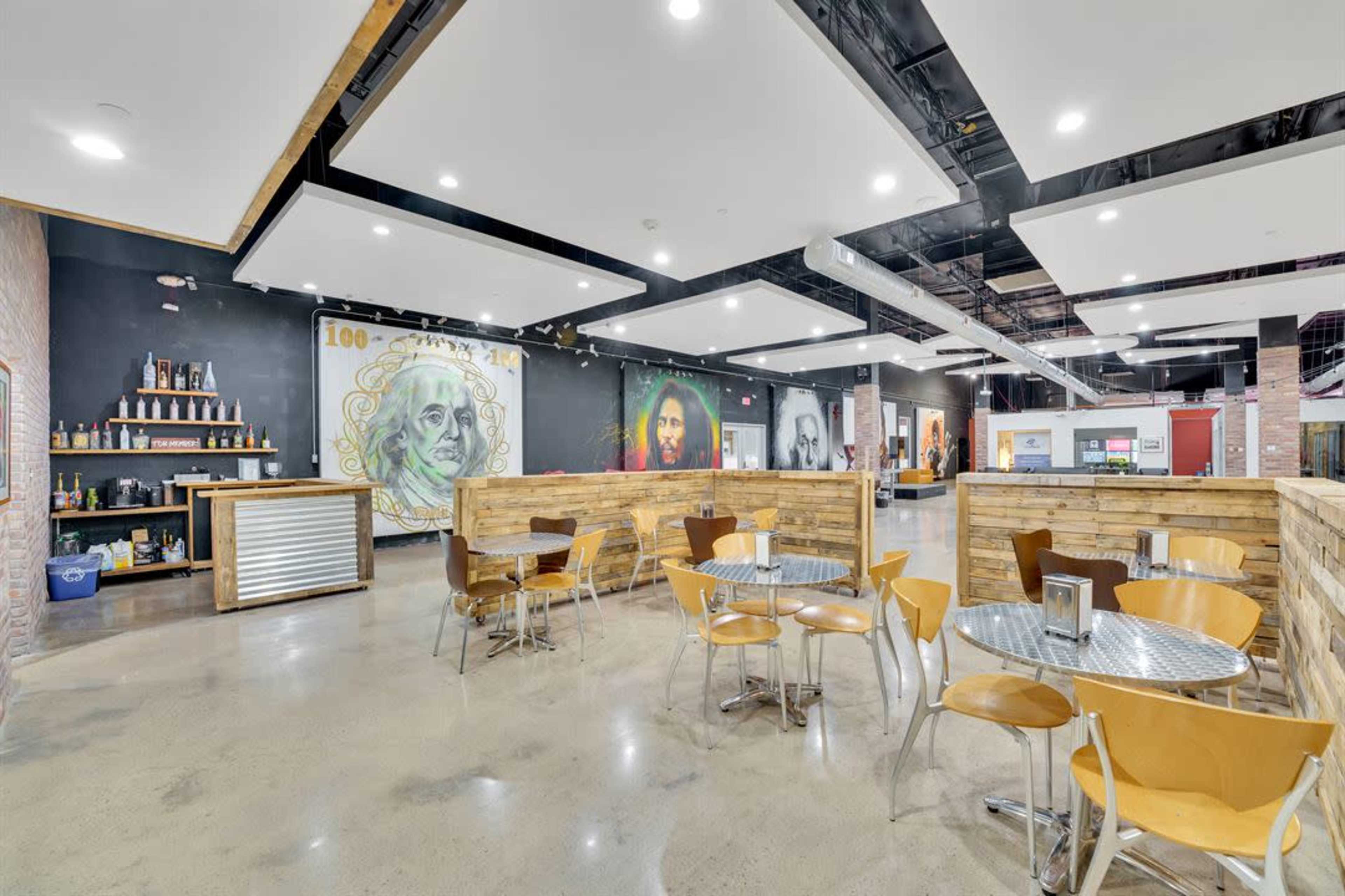 A modern café interior featuring wooden seating areas, a bar with shelves, and large murals on the walls.