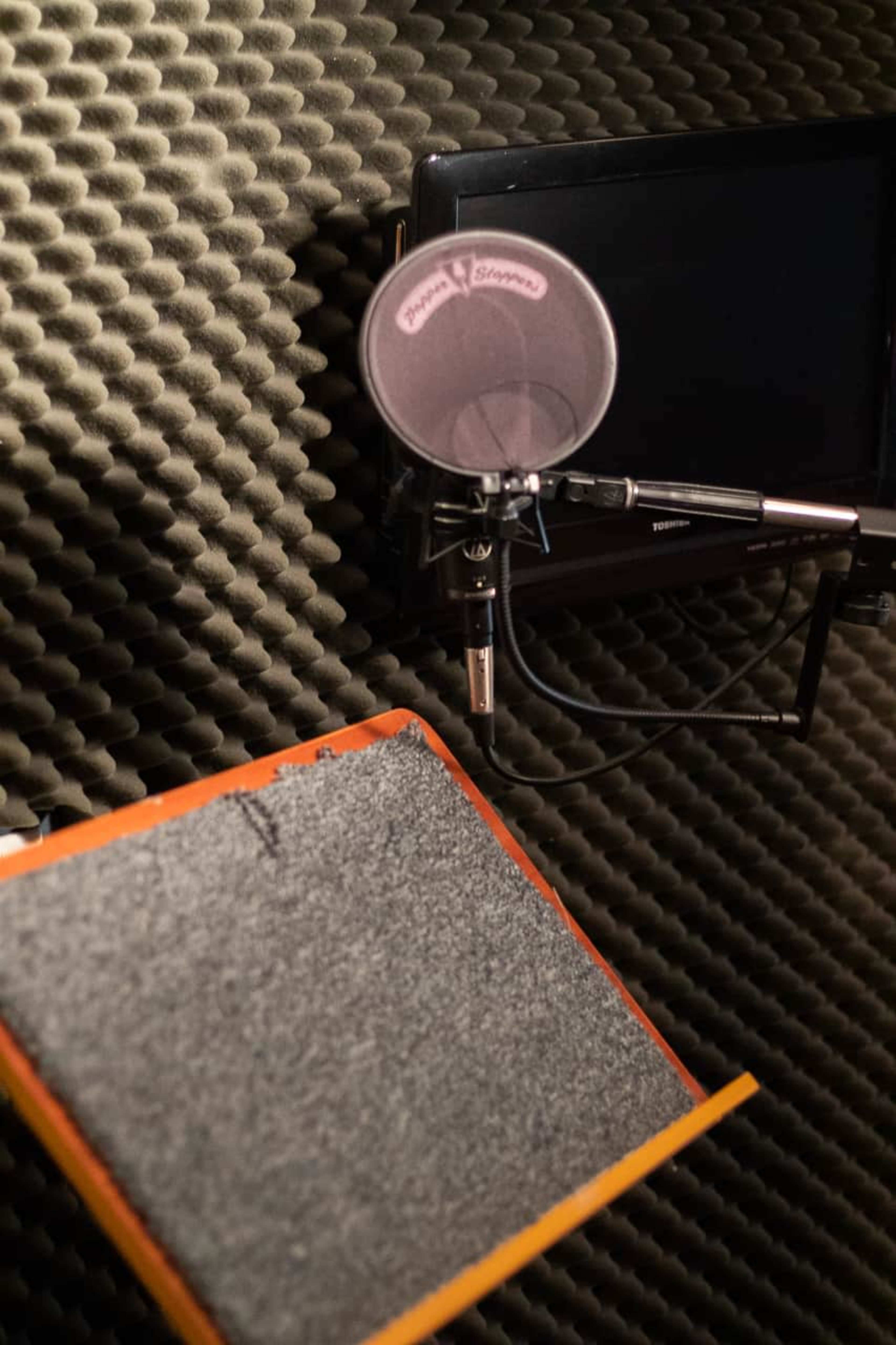 A microphone and a screen in a soundproof recording booth.