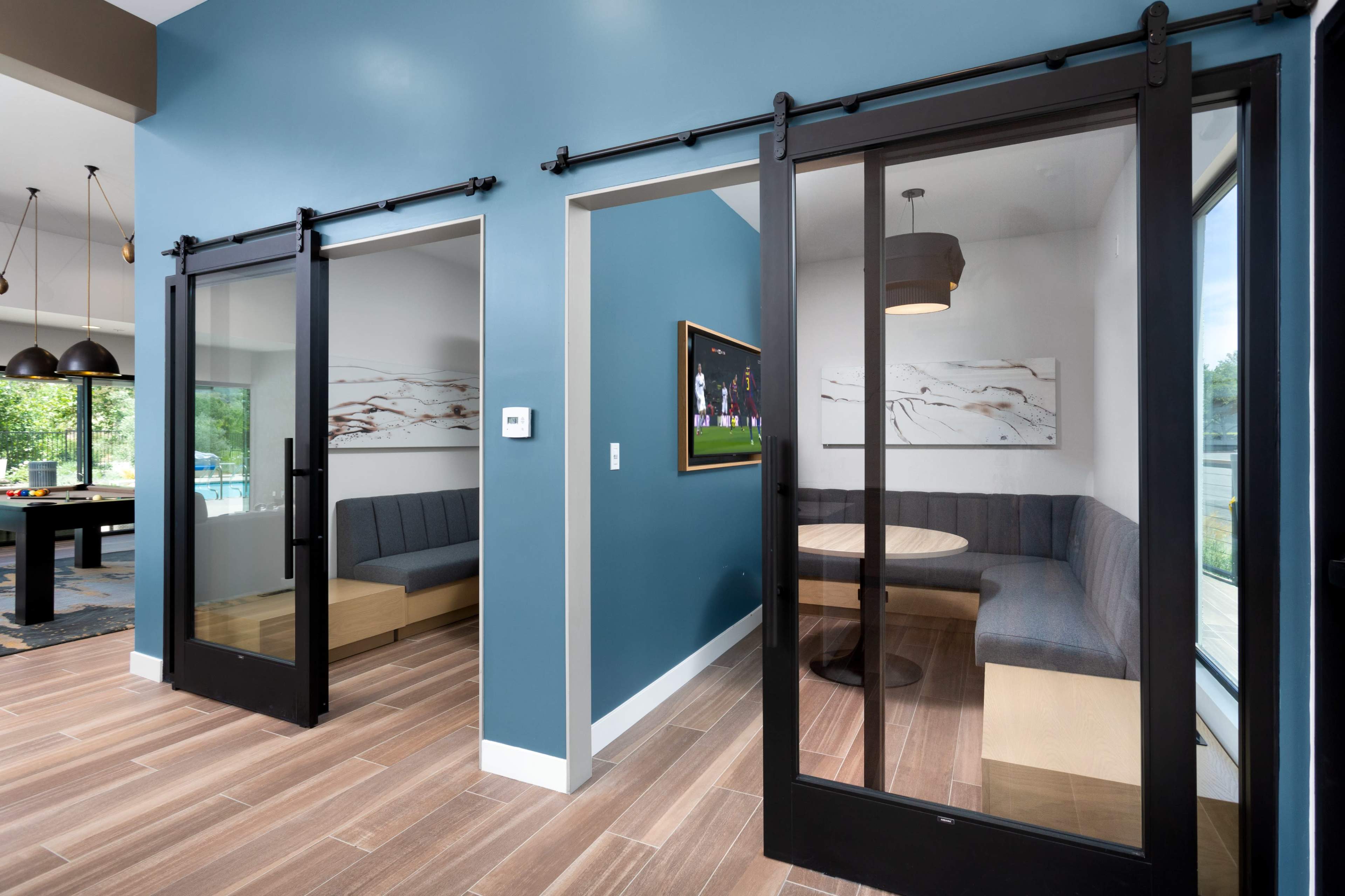 A modern interior space featuring two glass-fronted meeting rooms with dark accents and seating along the walls.