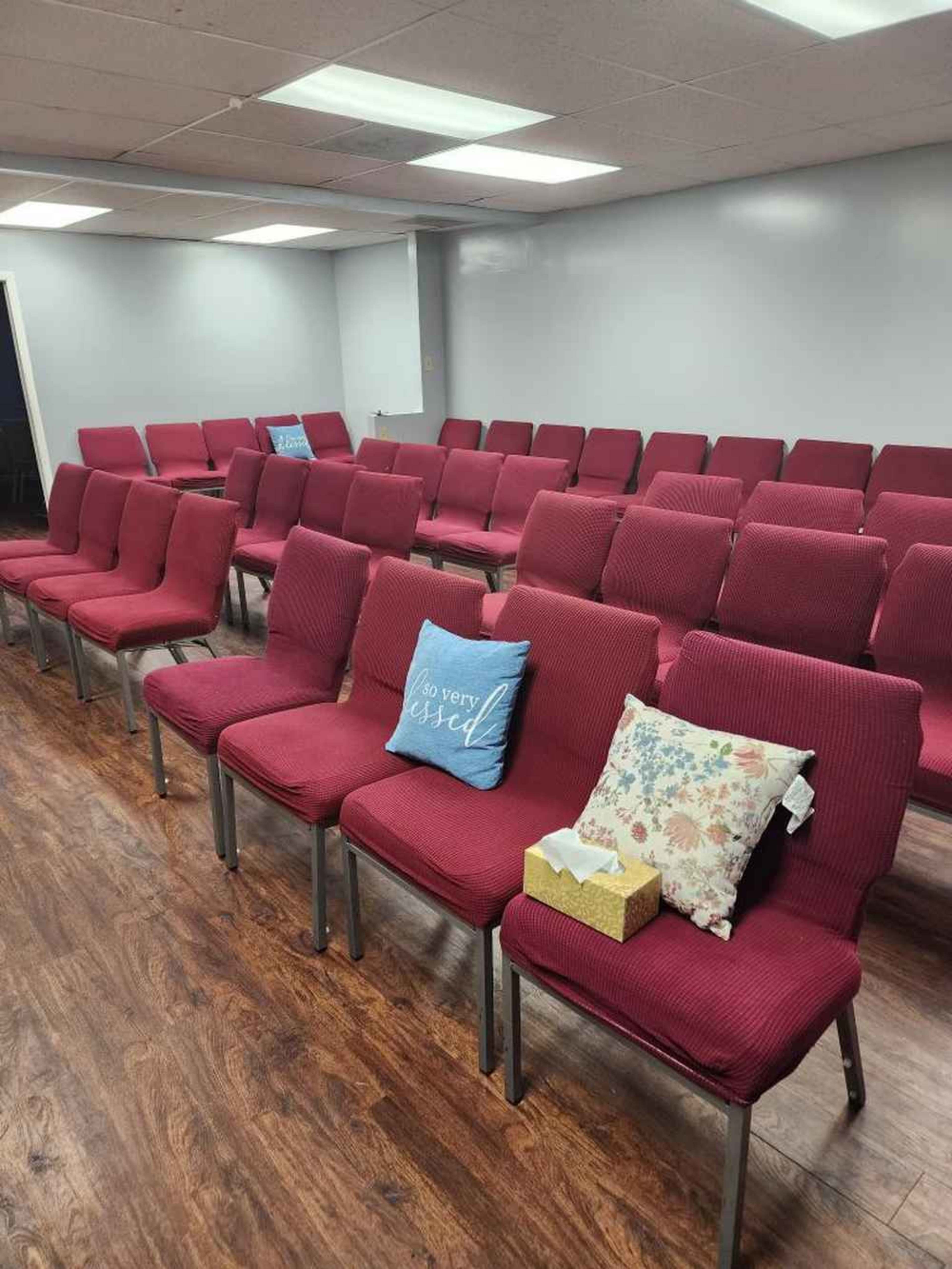 A set of red upholstered chairs arranged in rows in a well-lit room with wooden flooring.