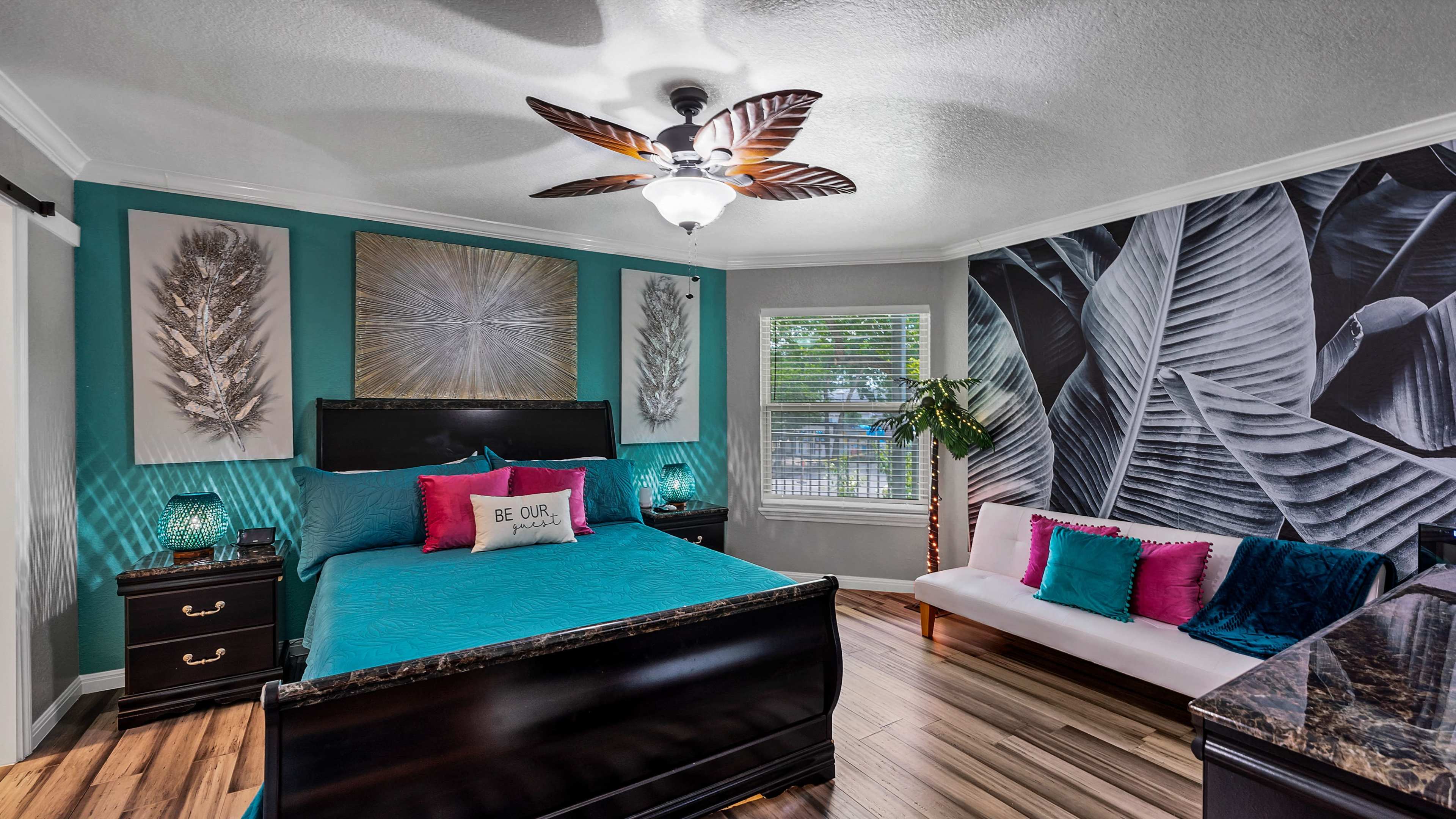 A well-decorated bedroom featuring a black bed with colorful pillows, a tropical-themed accent wall, and modern furnishings.