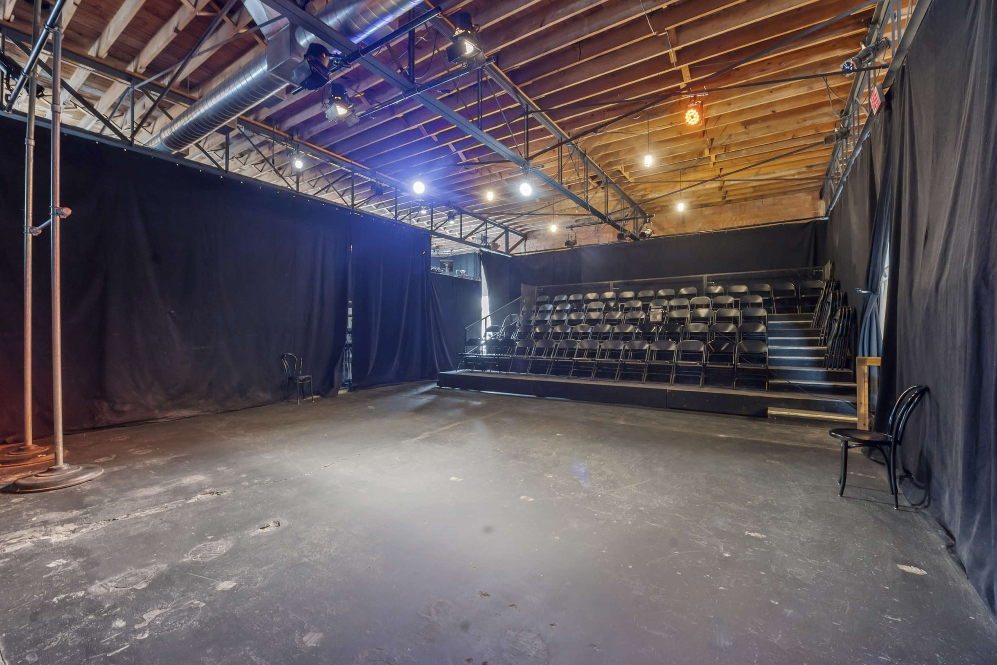 A spacious, theater-like room with black curtains, a tiered seating area, and a polished concrete floor.