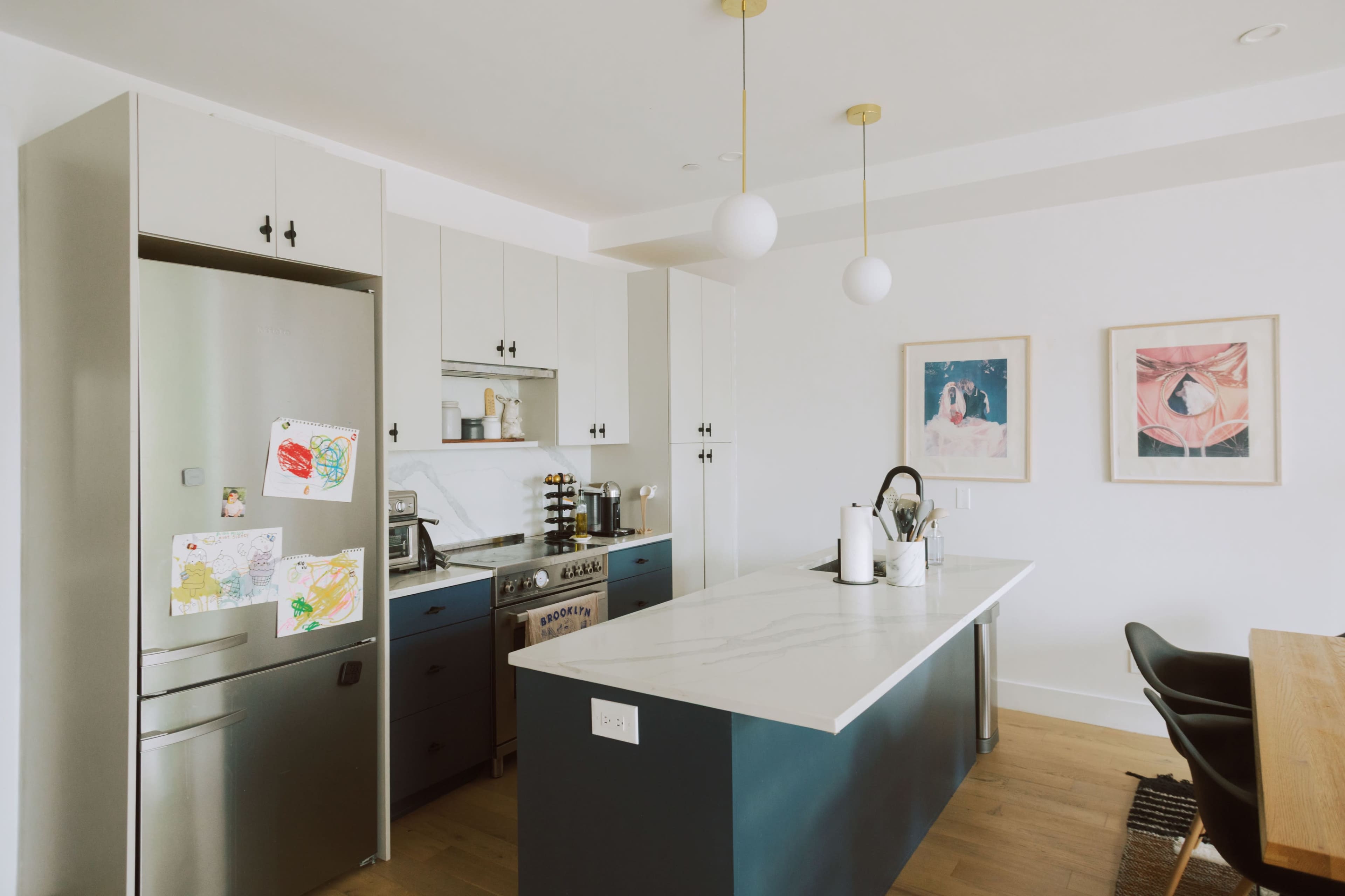 A modern kitchen features gray cabinetry, a large marble island, and artwork on the walls.