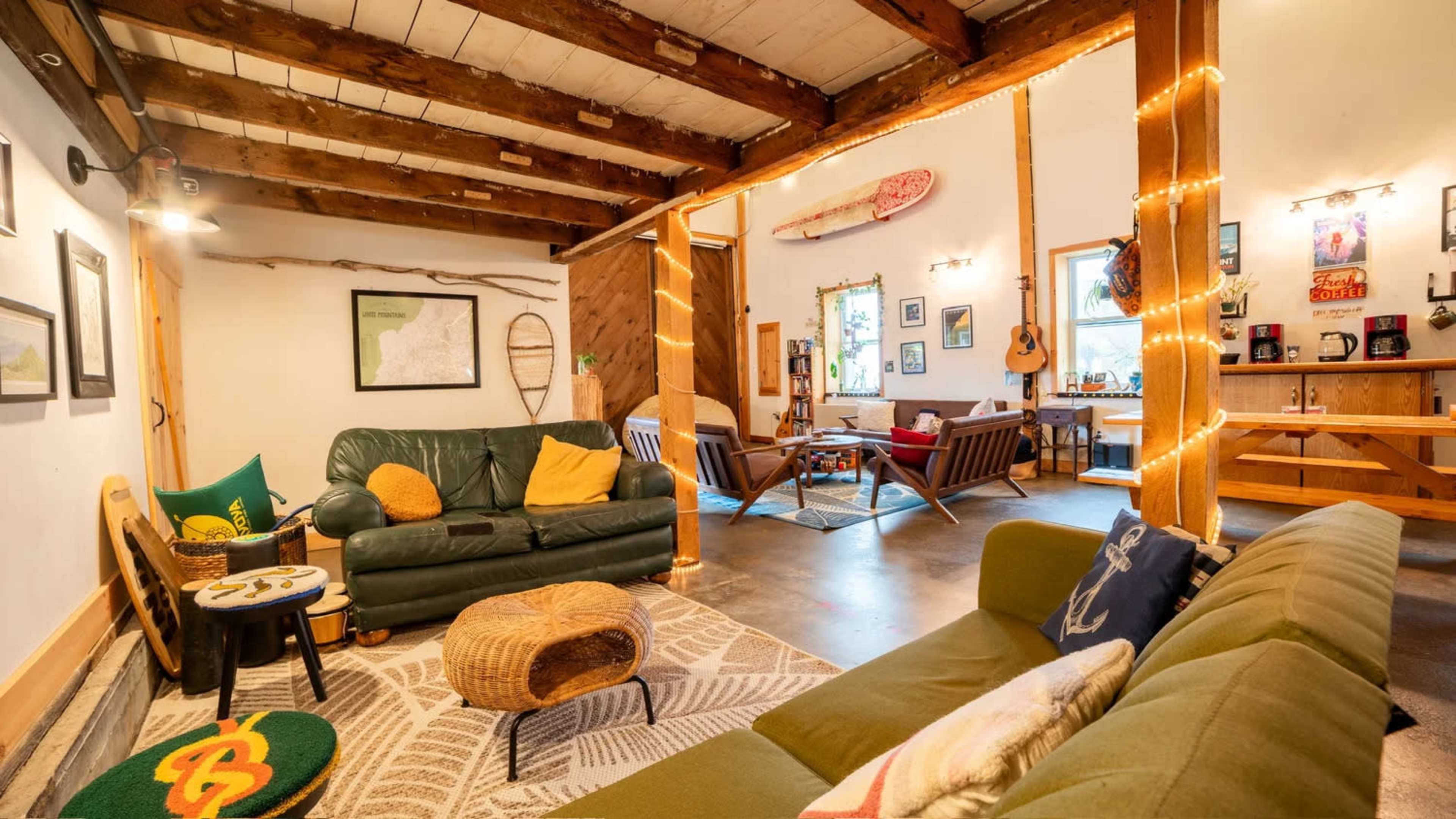 The image shows a cozy living space with a green sofa, wooden beams, and a blend of furniture including chairs and a coffee table, adorned with decorative lights.