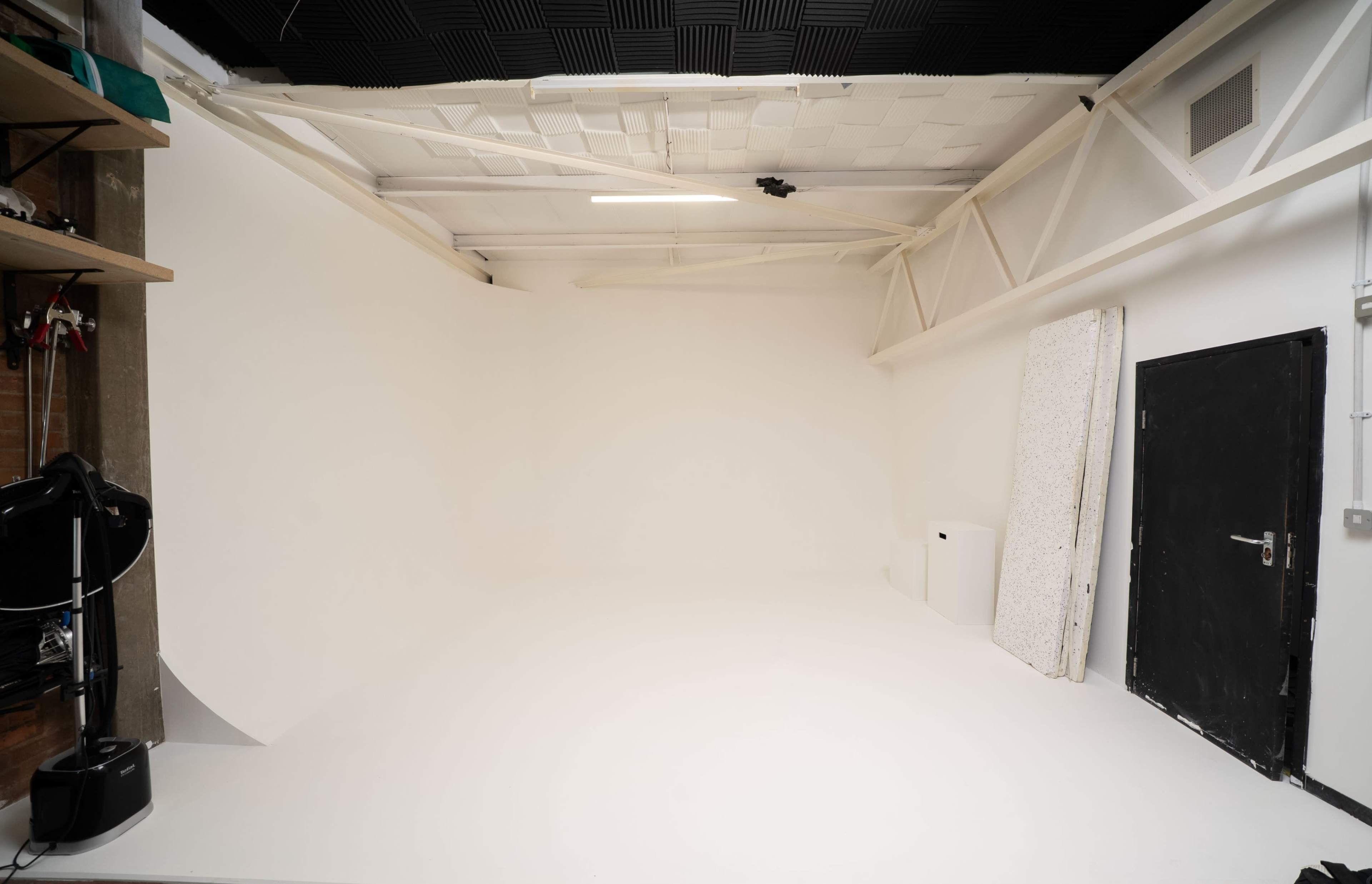 The image shows a large, empty photography studio with white walls and a seamless backdrop.