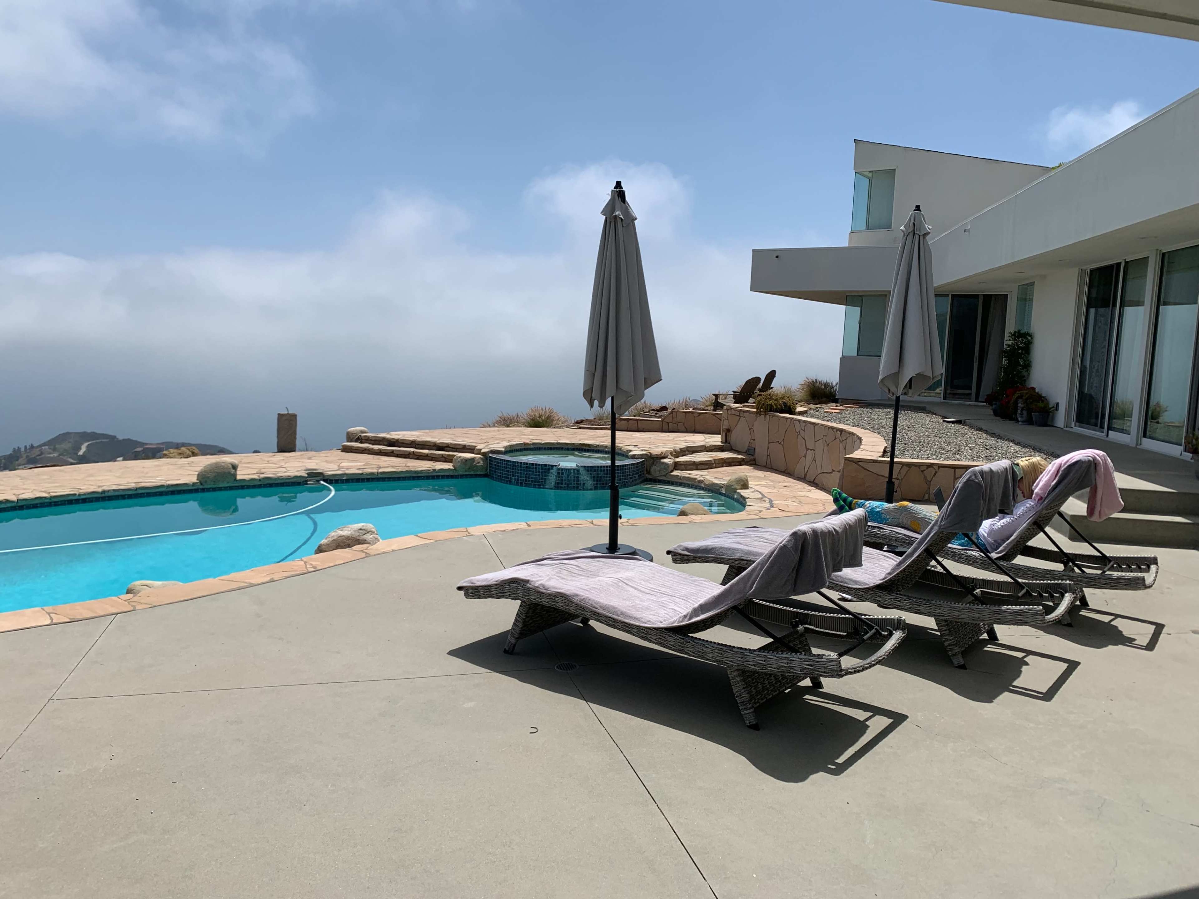 The image shows a swimming pool area with two lounge chairs and umbrellas, overlooking a distant foggy landscape.