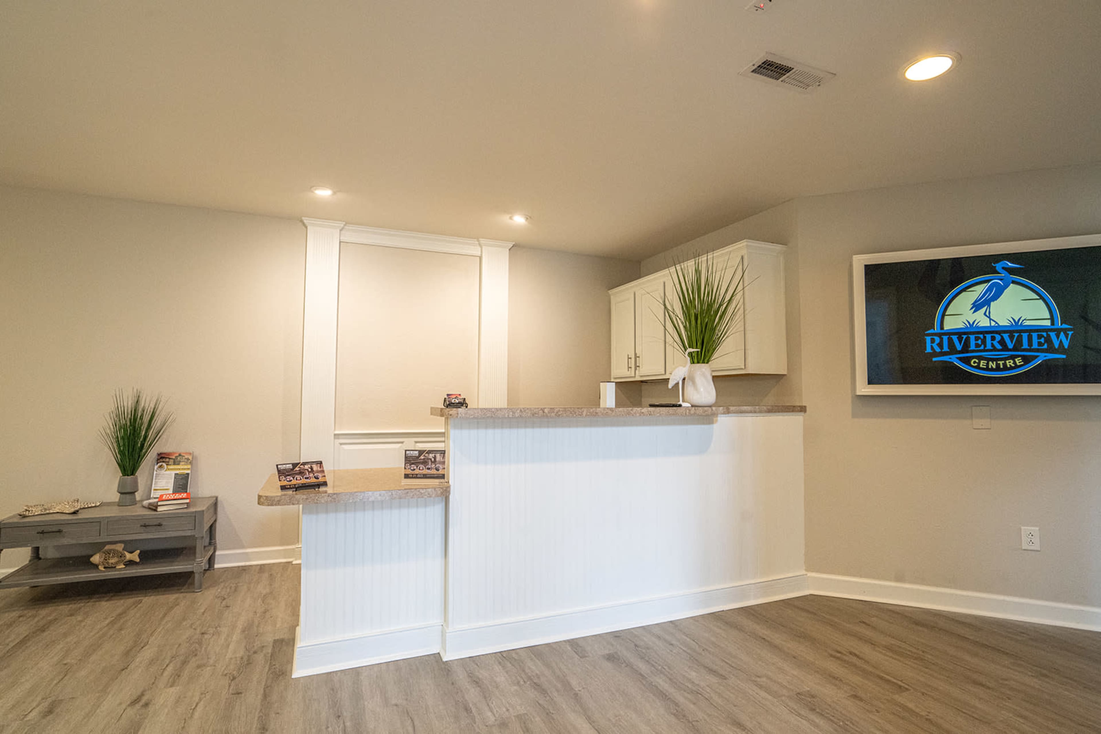 A modern reception area featuring a front desk, light-colored walls, and a TV displaying the "Riverview Centre" logo.