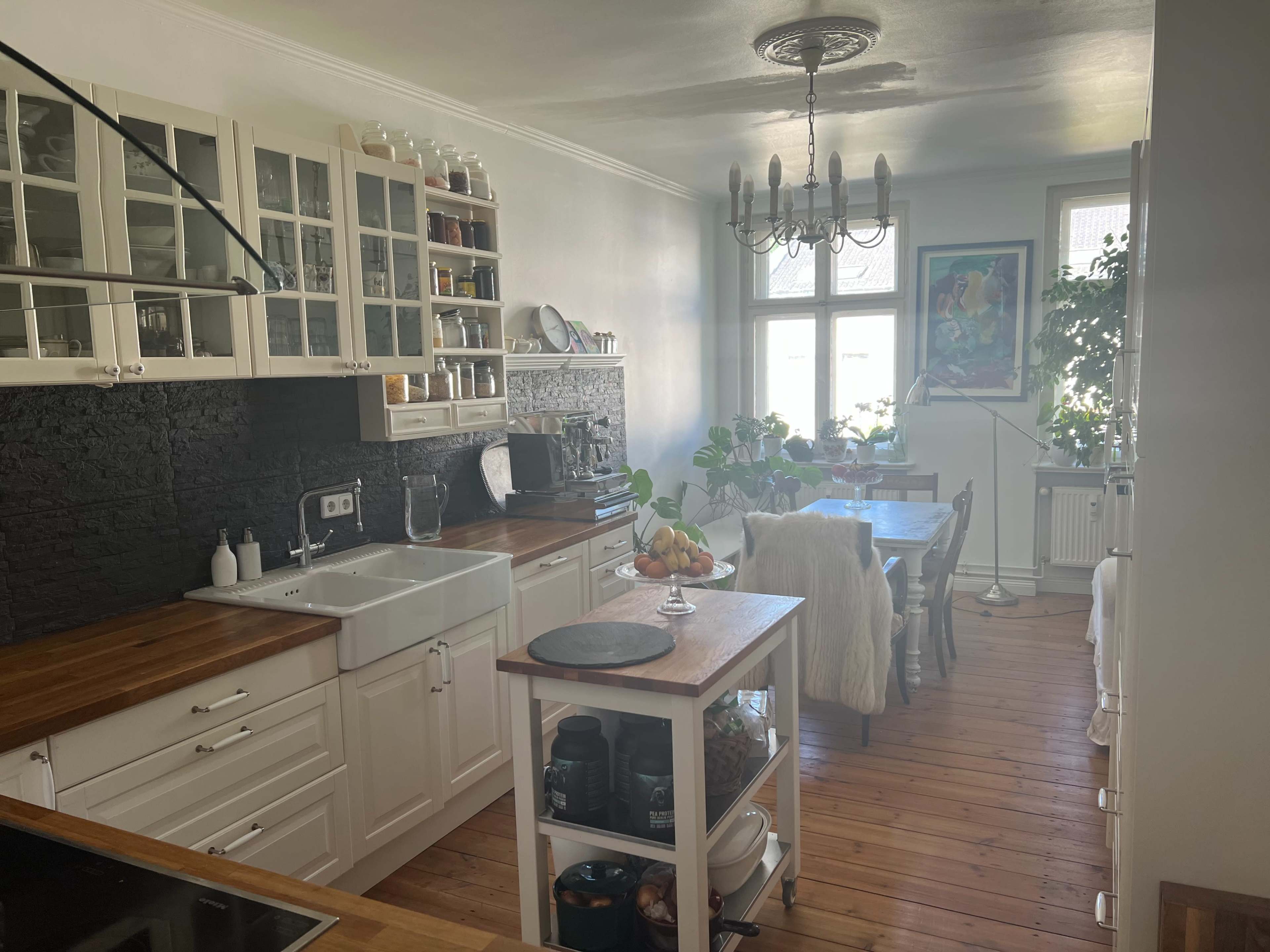 A bright kitchen with white cabinetry, a farmhouse sink, and a wooden dining table surrounded by chairs.