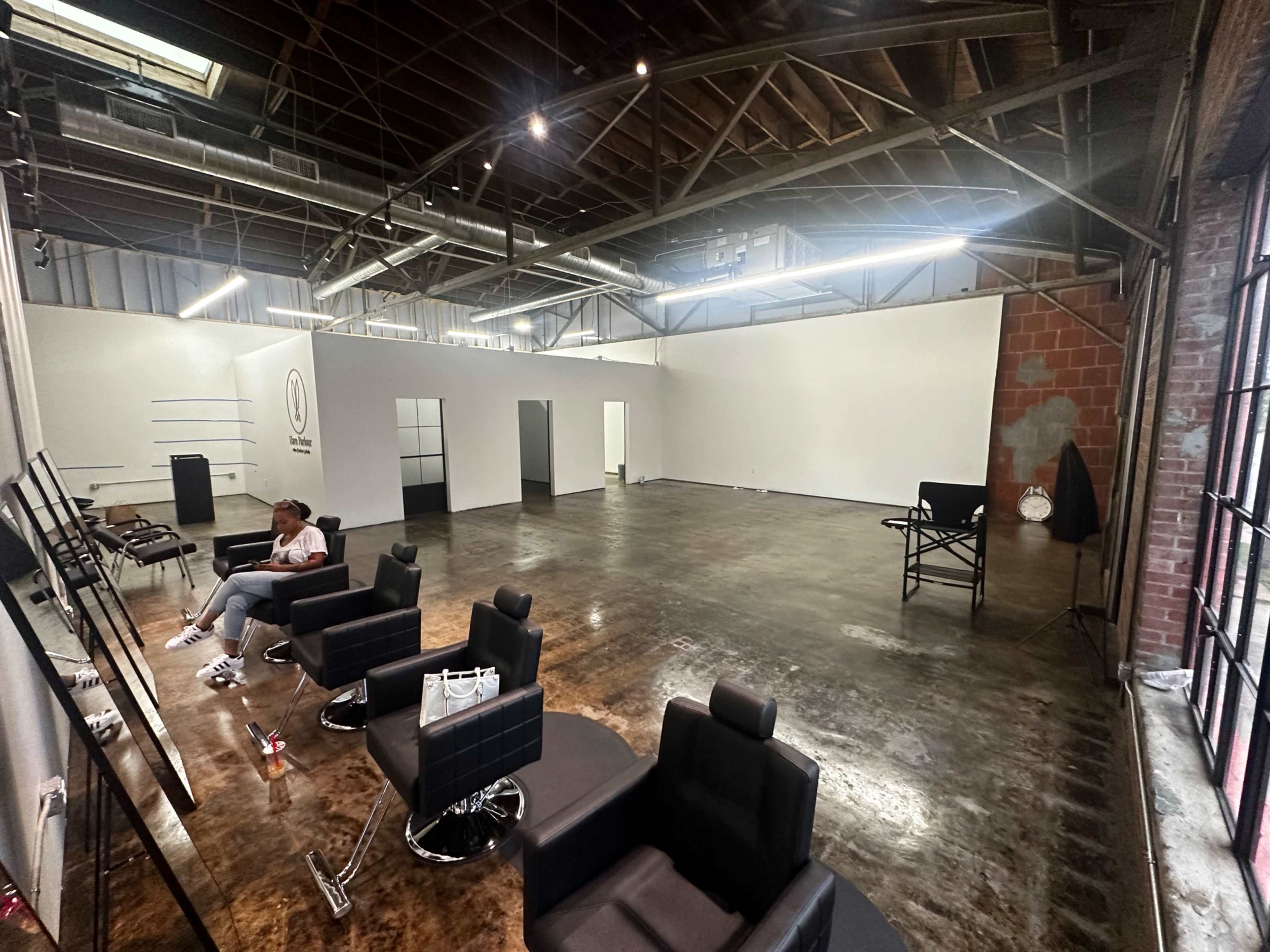 An empty hair salon with black styling chairs, large mirrors, and exposed wooden beams overhead.