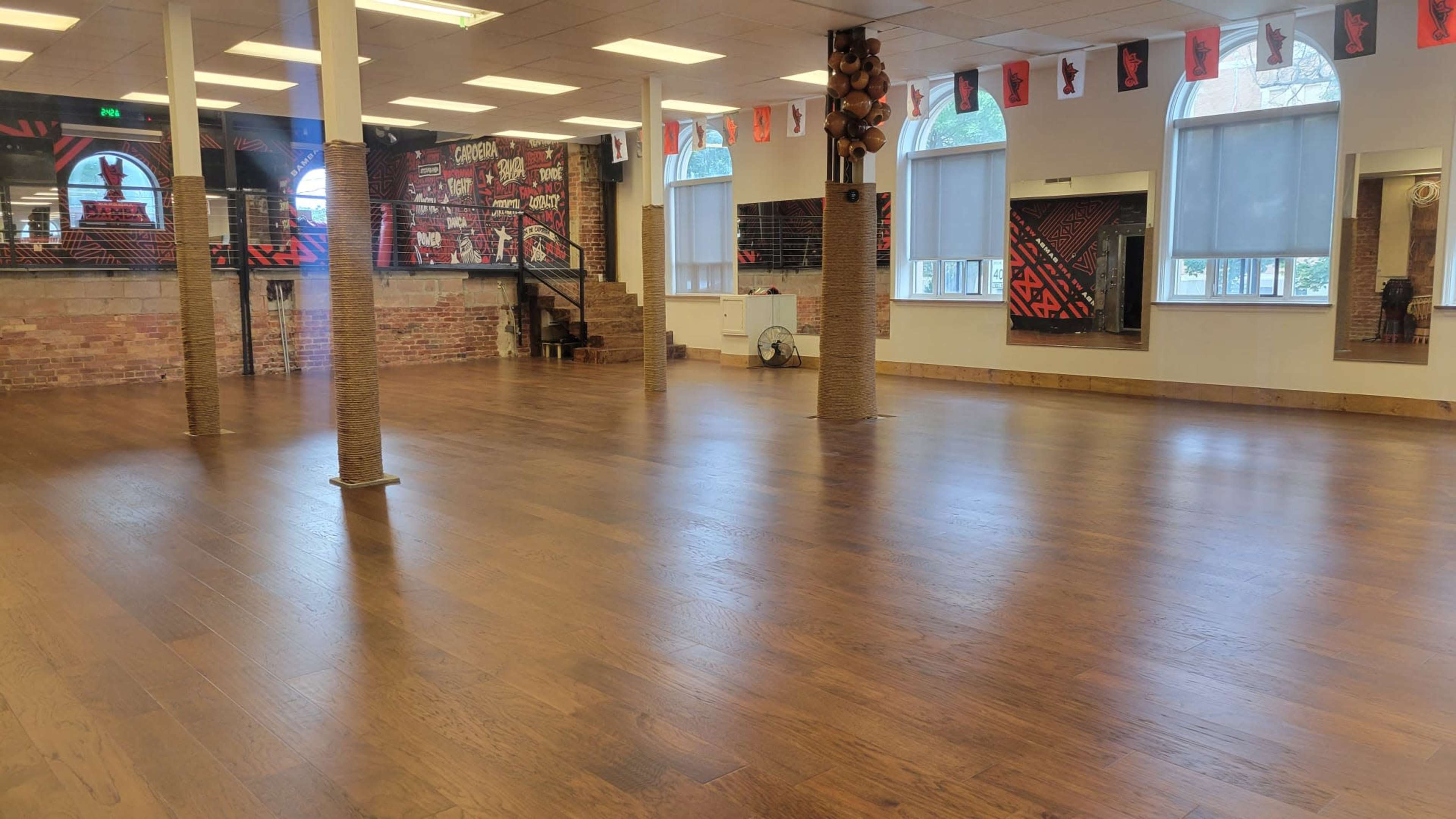 The image shows a spacious room with wooden flooring, large windows, and decorated walls featuring a red and black mural.