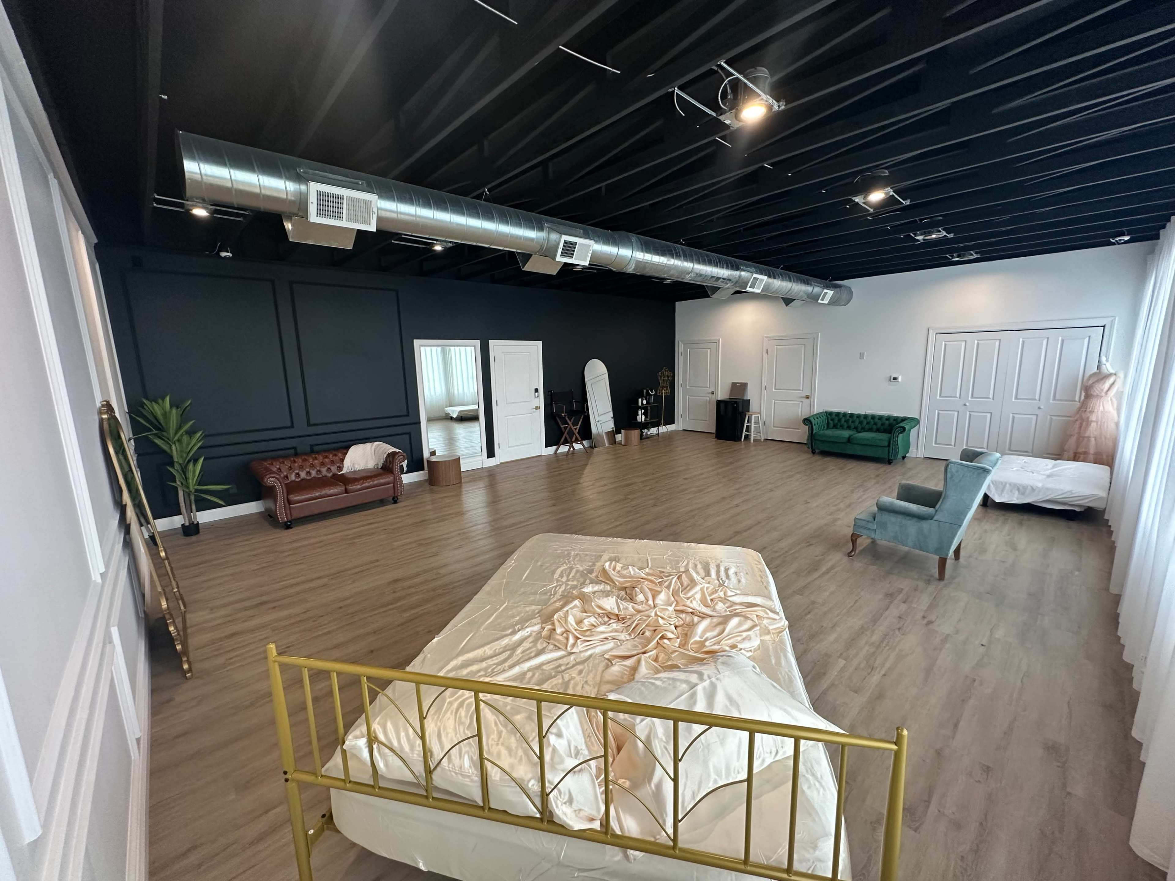 A spacious room with wooden flooring, featuring two beds, a green sofa, a brown couch, and a large mirror against the wall.
