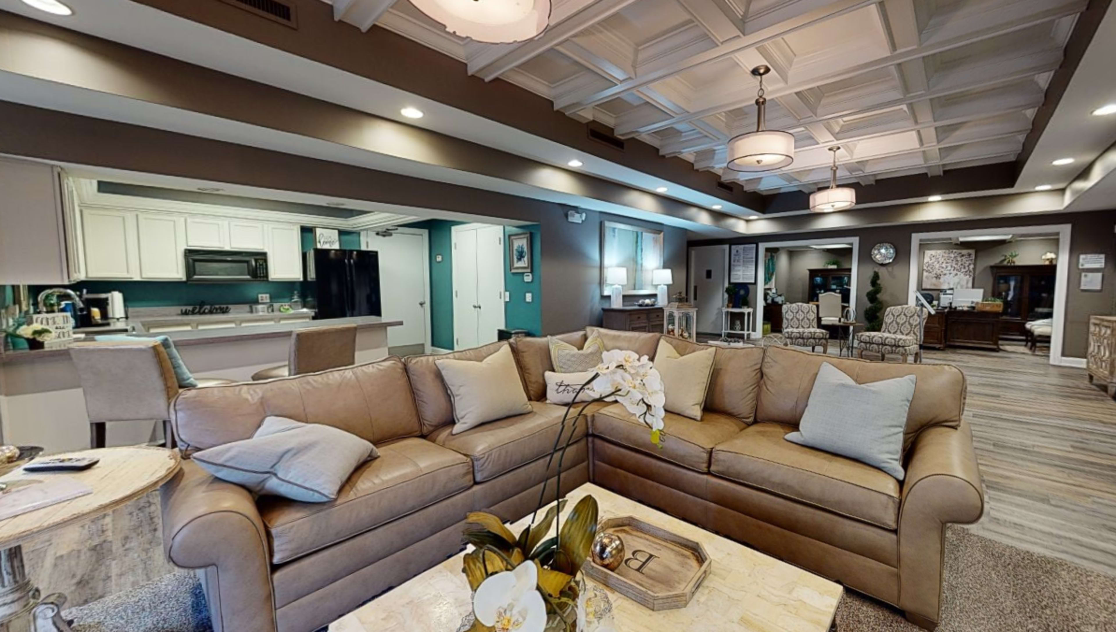 A modern living room with a beige sectional sofa, a coffee table adorned with decorative items, and a view of an open kitchen in the background.