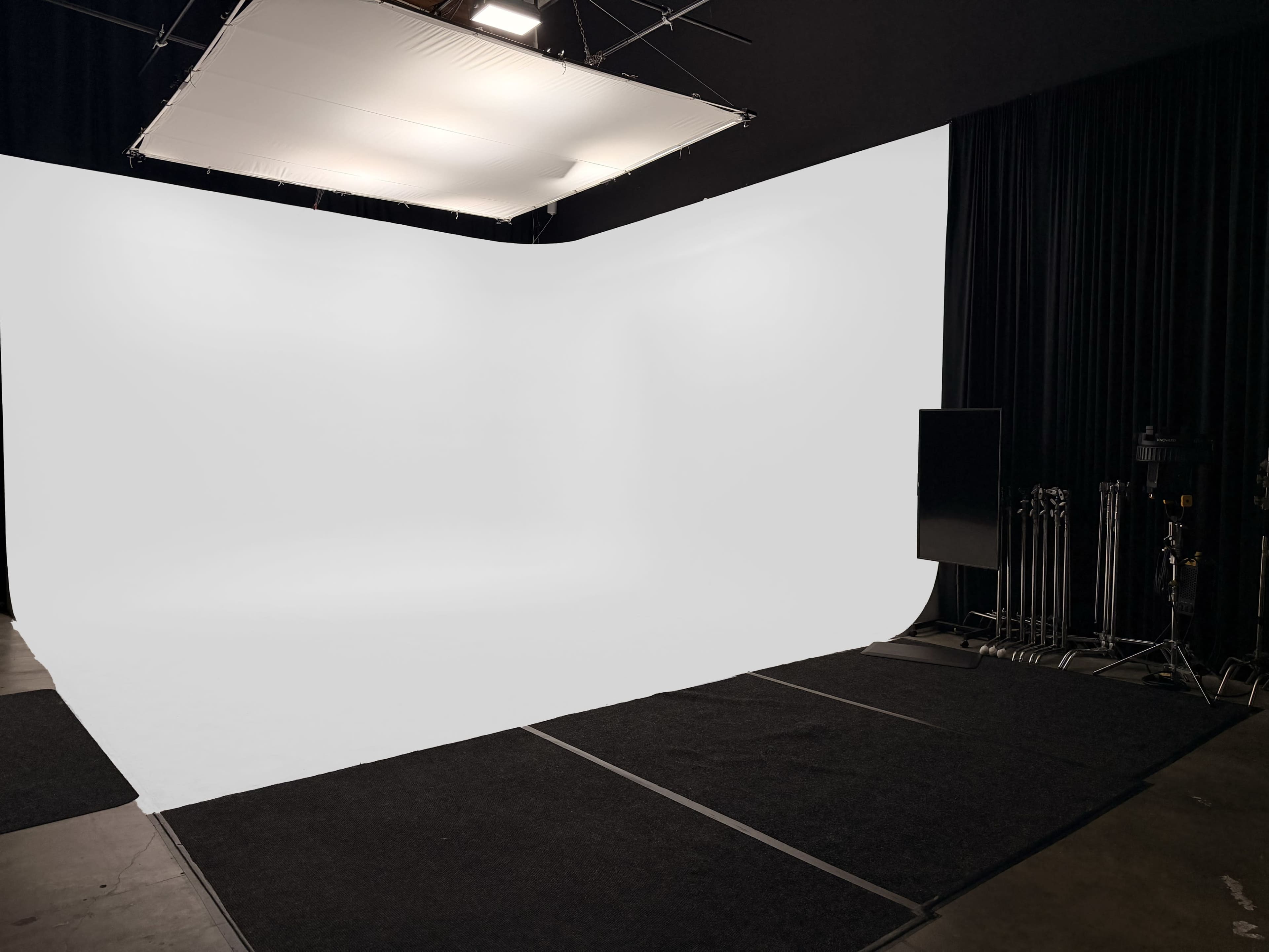 The image shows a photography studio with a large white backdrop and soft lighting setup, along with equipment stored on the side.