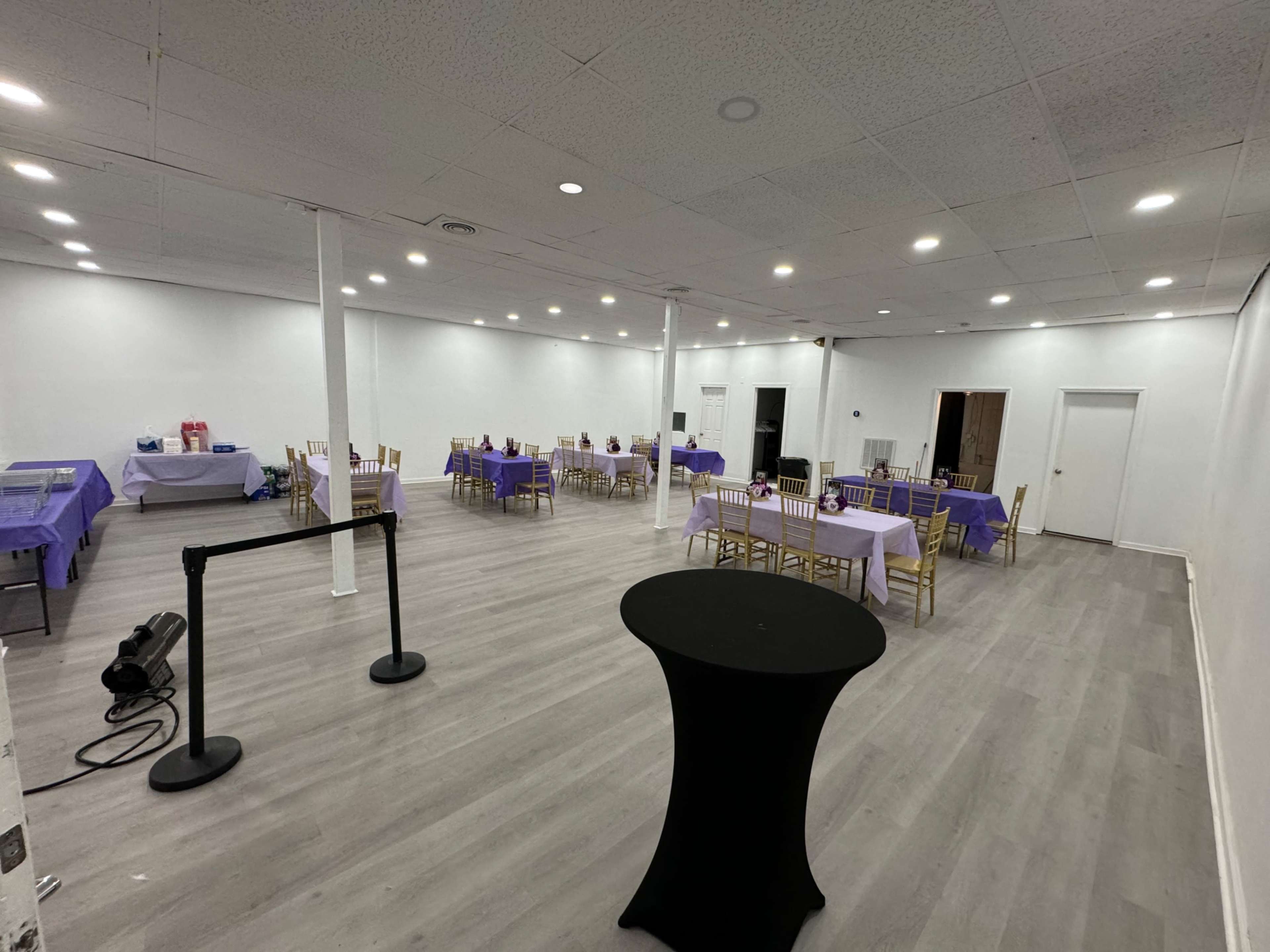 A spacious, empty event room with several tables covered in purple tablecloths and arranged with gold chairs.