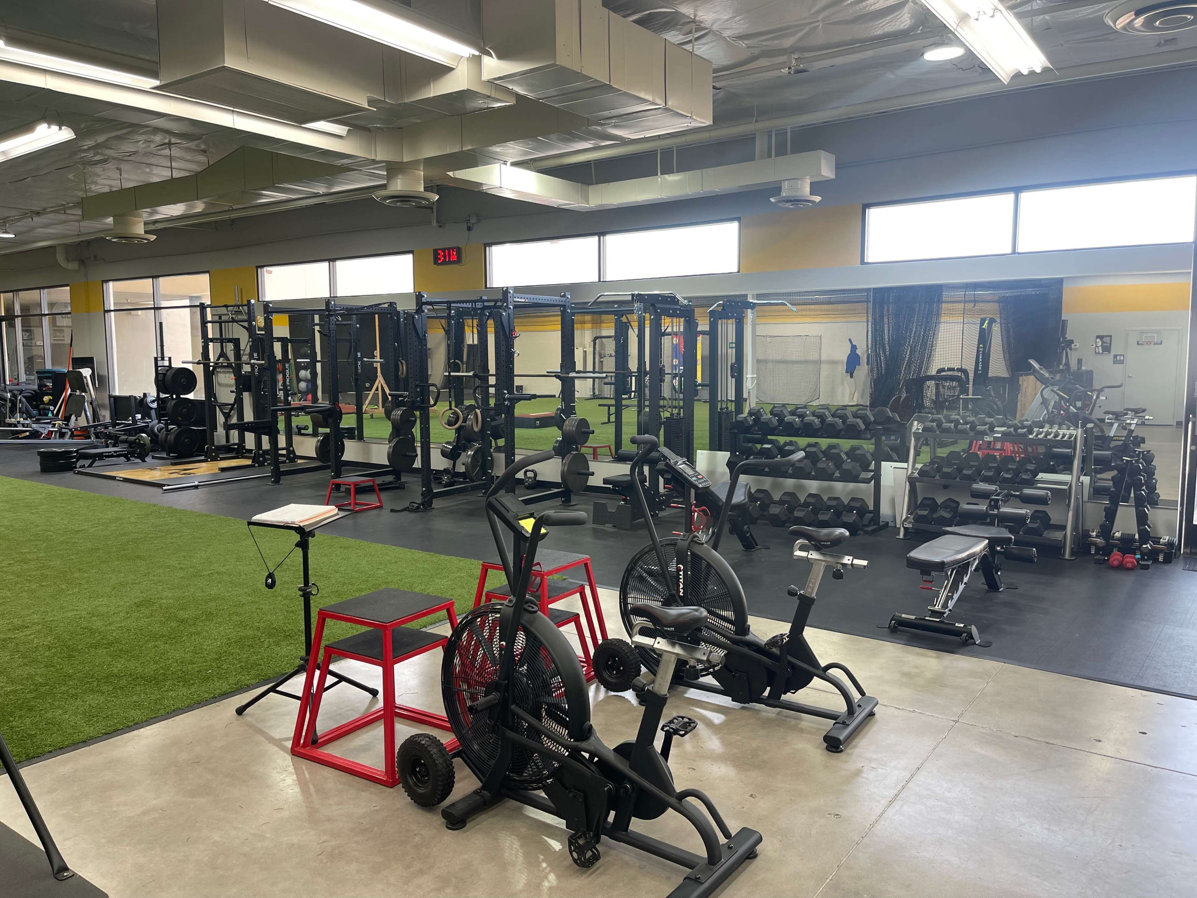 A well-equipped gym featuring various fitness machines, free weights, and a turf area for workouts.