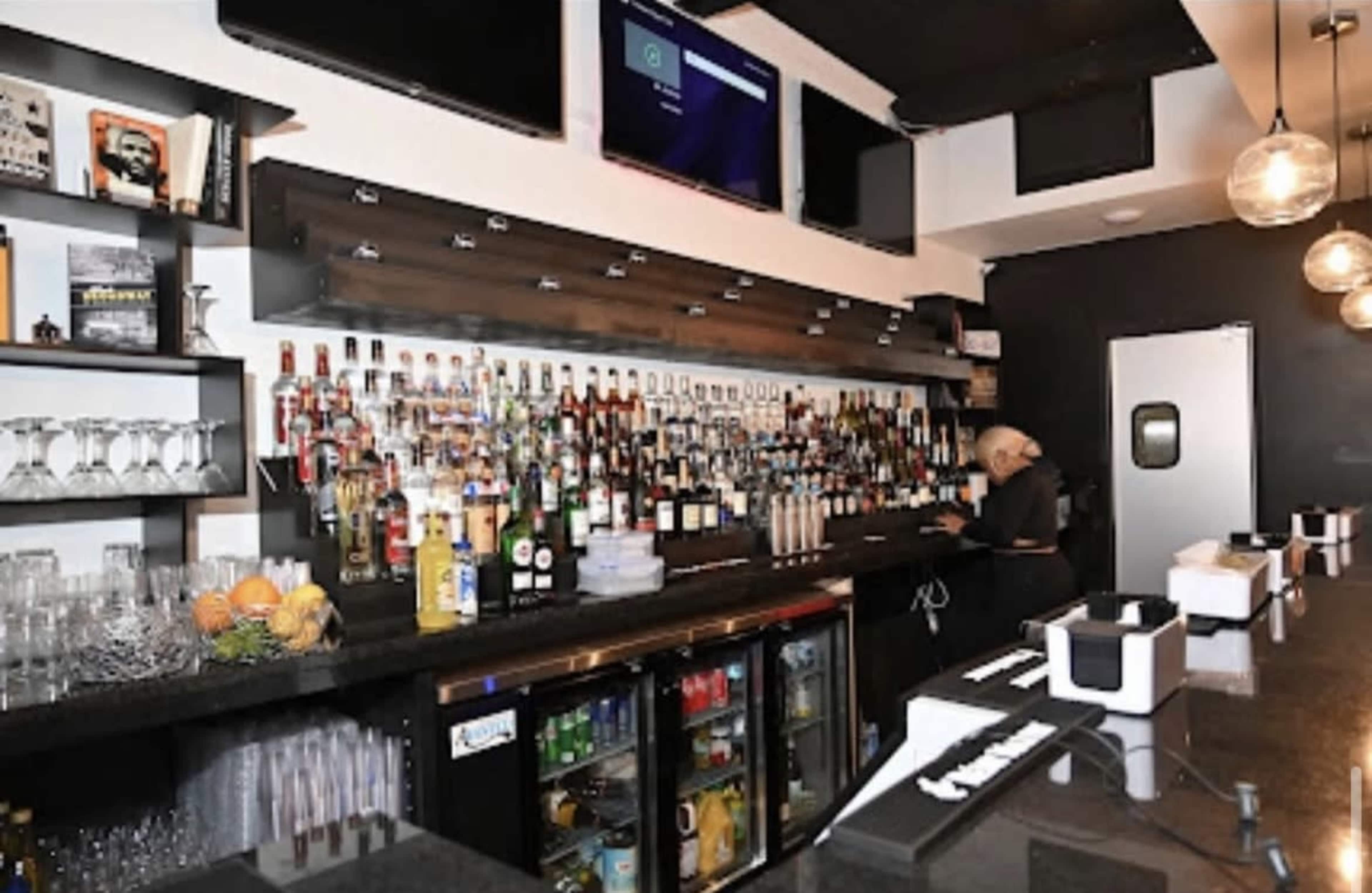 A well-stocked bar with various bottles of liquor on shelves and an employee preparing drinks behind the counter.