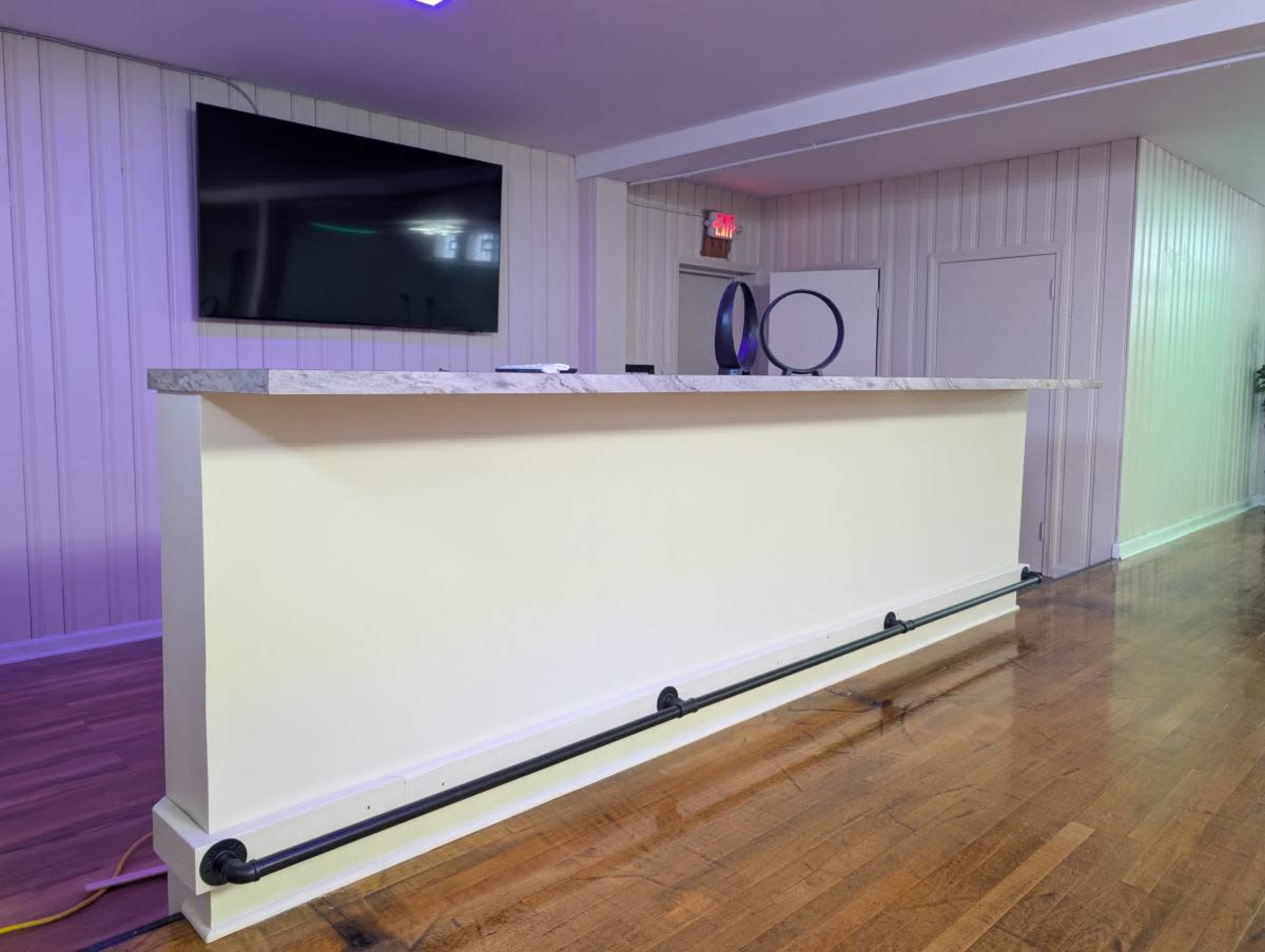 The image shows a modern reception desk with a marble countertop, situated in a well-lit room featuring wooden flooring and a mounted television on the wall.