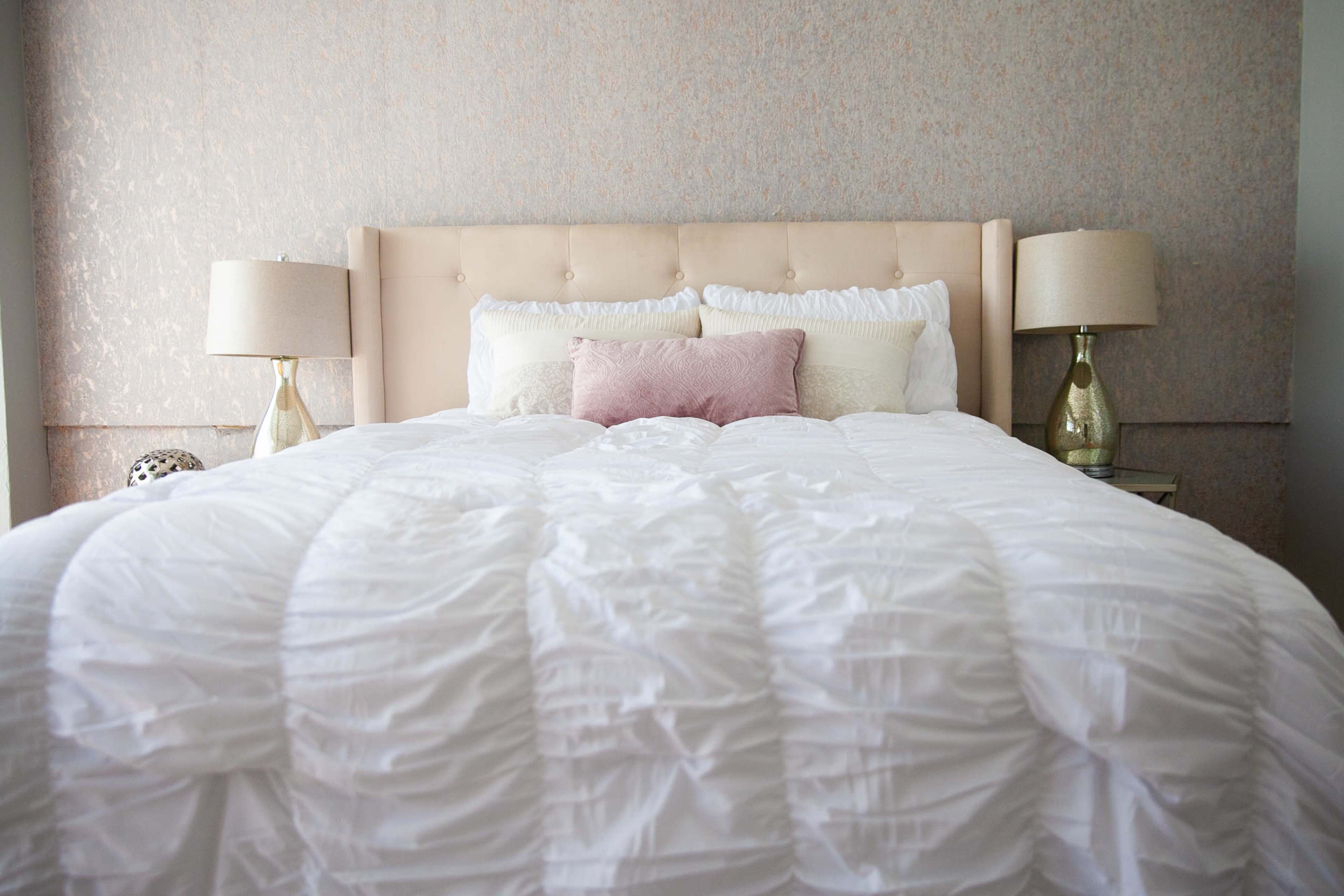 A neatly made bed with a tufted headboard is flanked by two bedside lamps on a softly patterned wall.