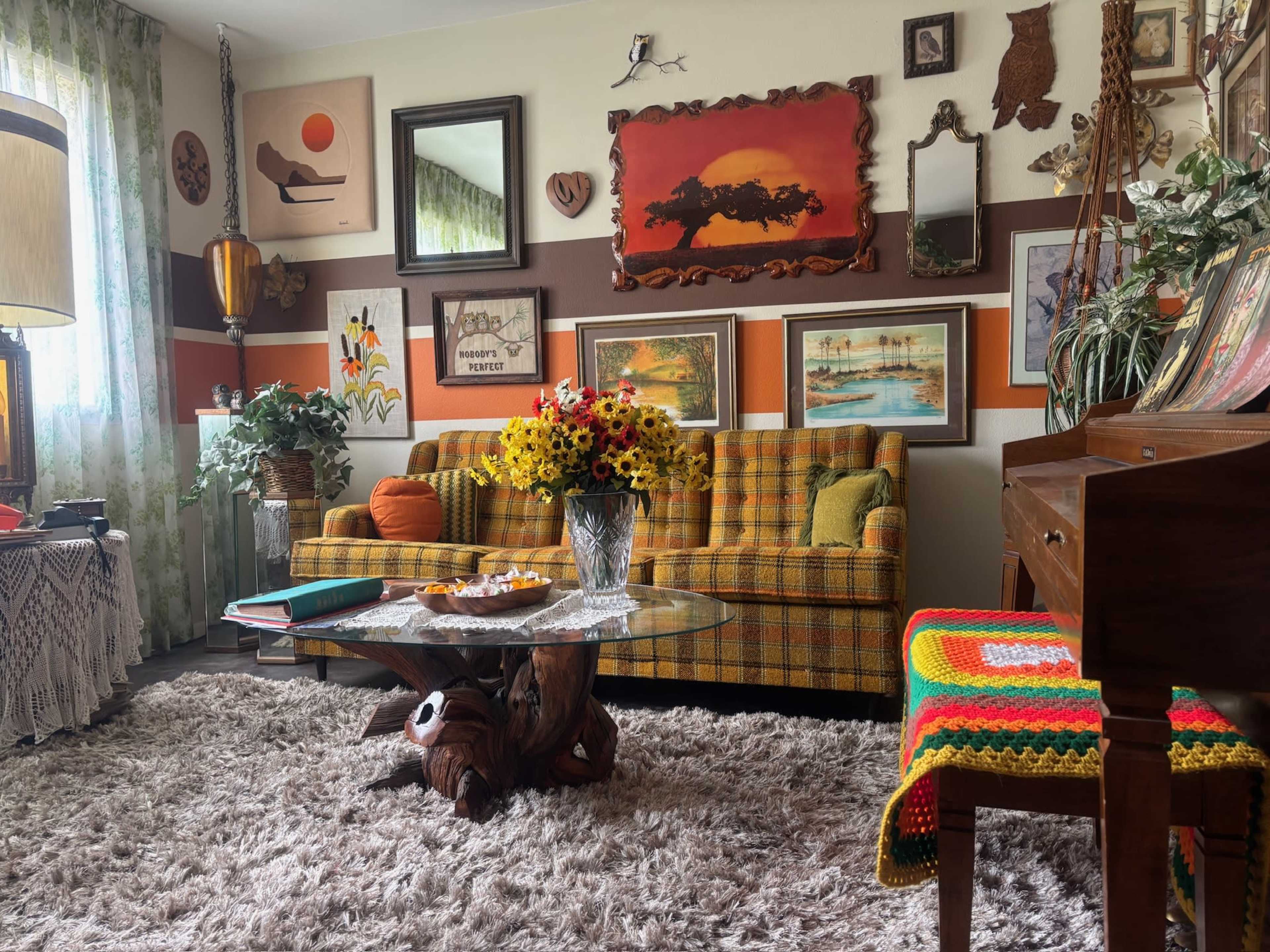 The living room features a vintage-style couch with a patterned design, a glass coffee table, and various framed artworks on the walls.
