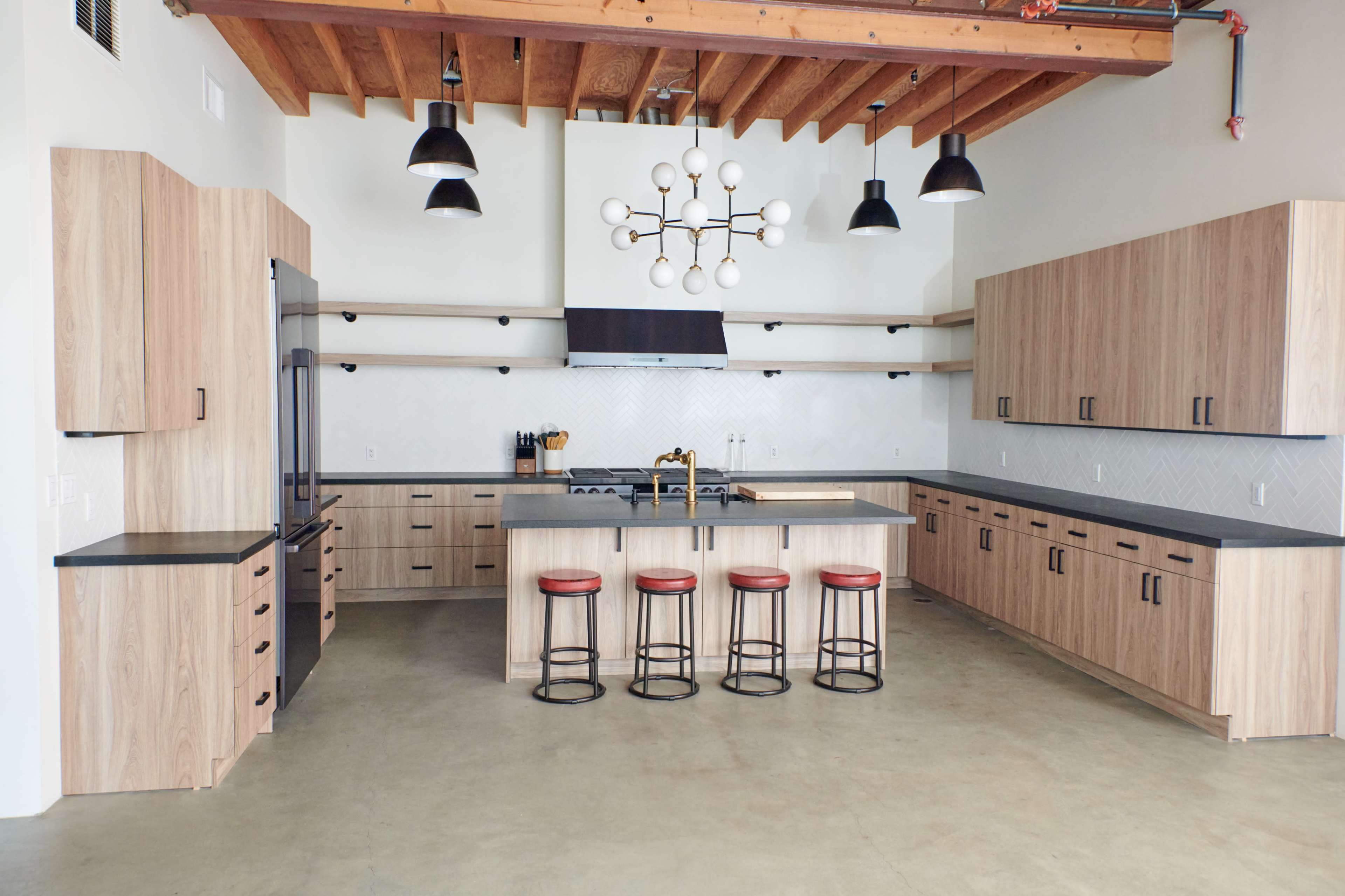A modern kitchen features wooden cabinetry, a large island with stools, and a minimalist lighting fixture overhead.
