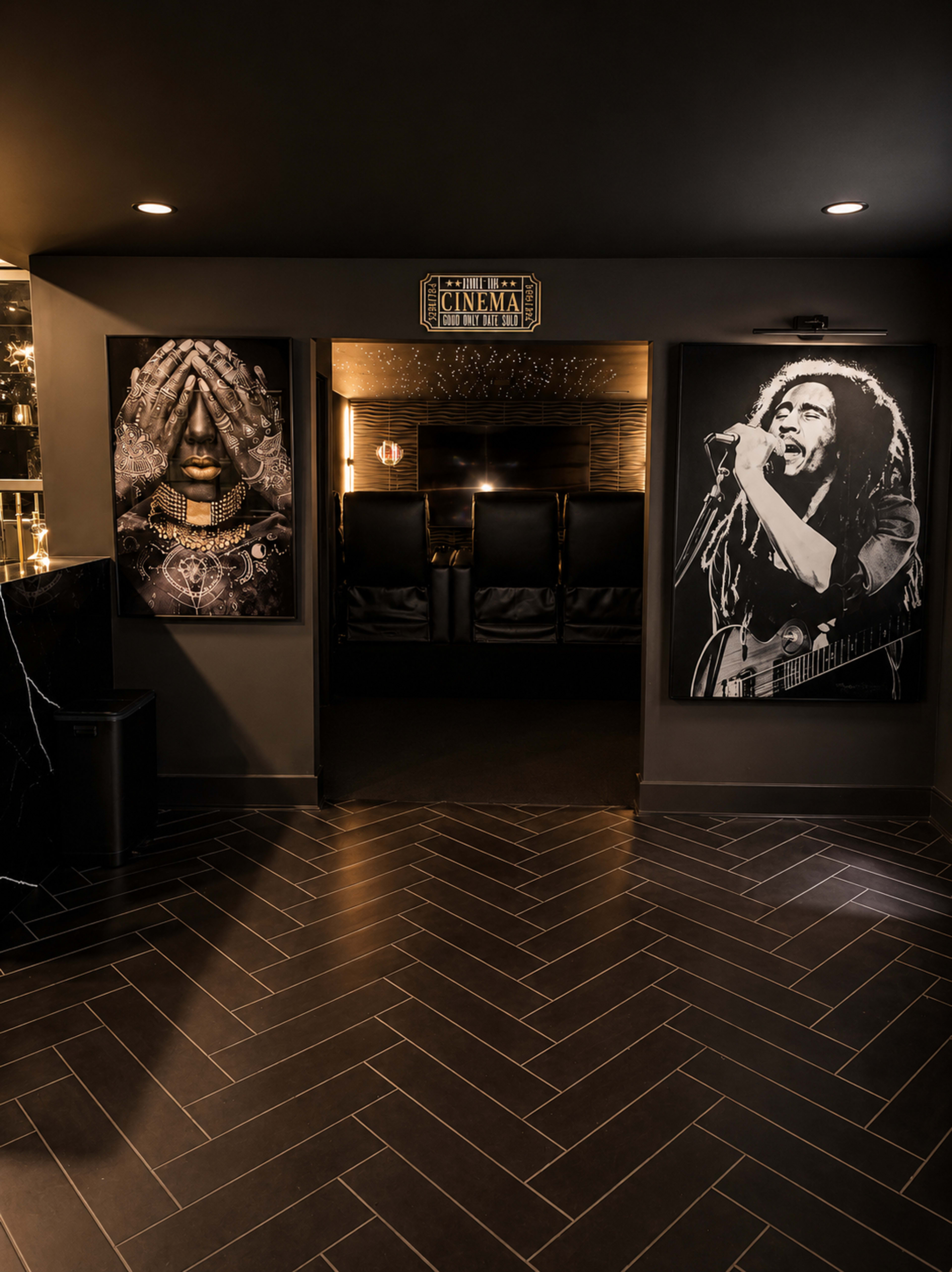 The image shows a hallway leading to a cinema, featuring two large framed portraits on the walls: one of a woman with her hands covering her face and the other of a man playing a guitar.