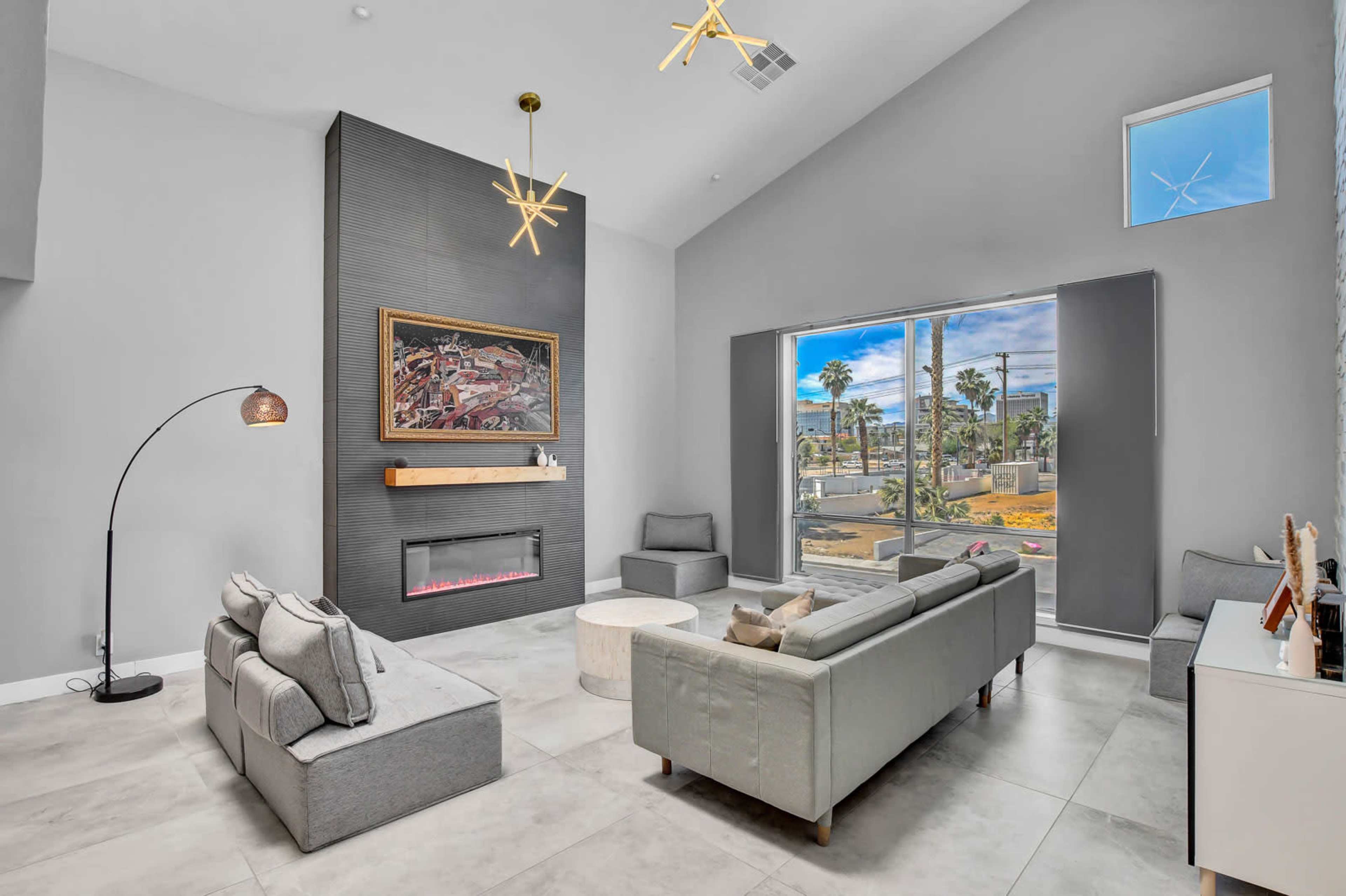 The living room features a modern design with a large window, artwork on the wall, and a sleek fireplace.