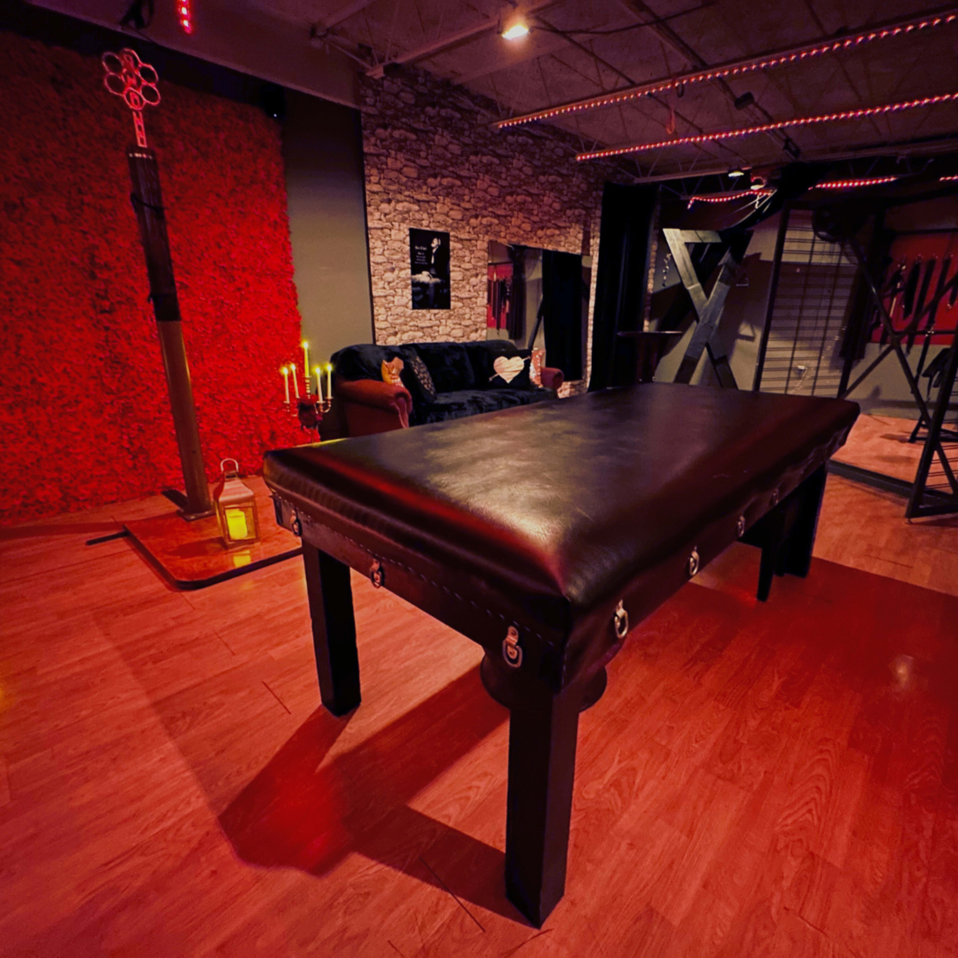 The image shows a dimly lit room featuring a large black table, a couch, and various objects that suggest a themed interior design.