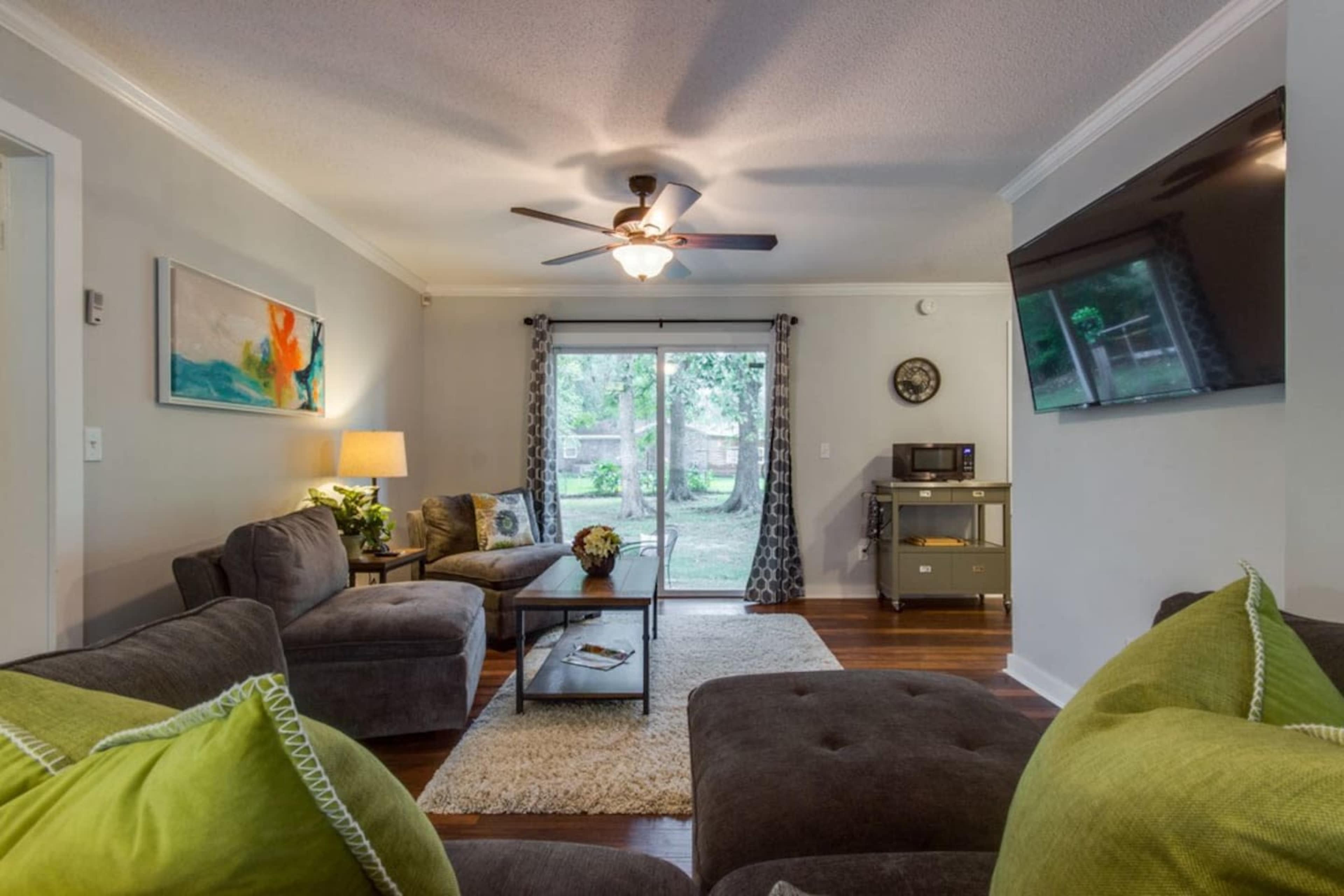 The living room features a sofa, armchair, and coffee table positioned around a large window that opens to a view of a backyard.