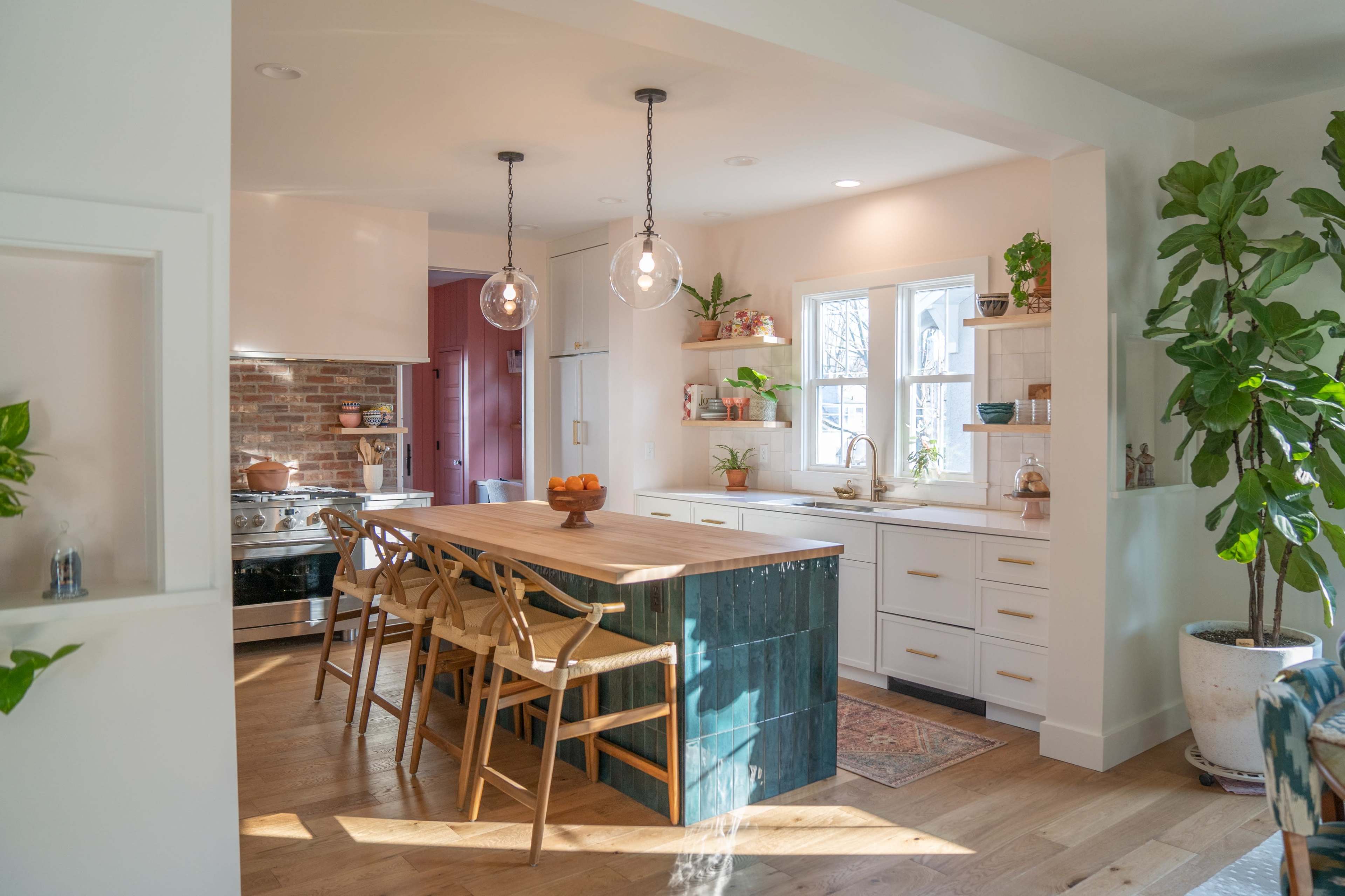 A modern kitchen features a large wooden island with seating, white cabinetry, and an accent wall of exposed brick.