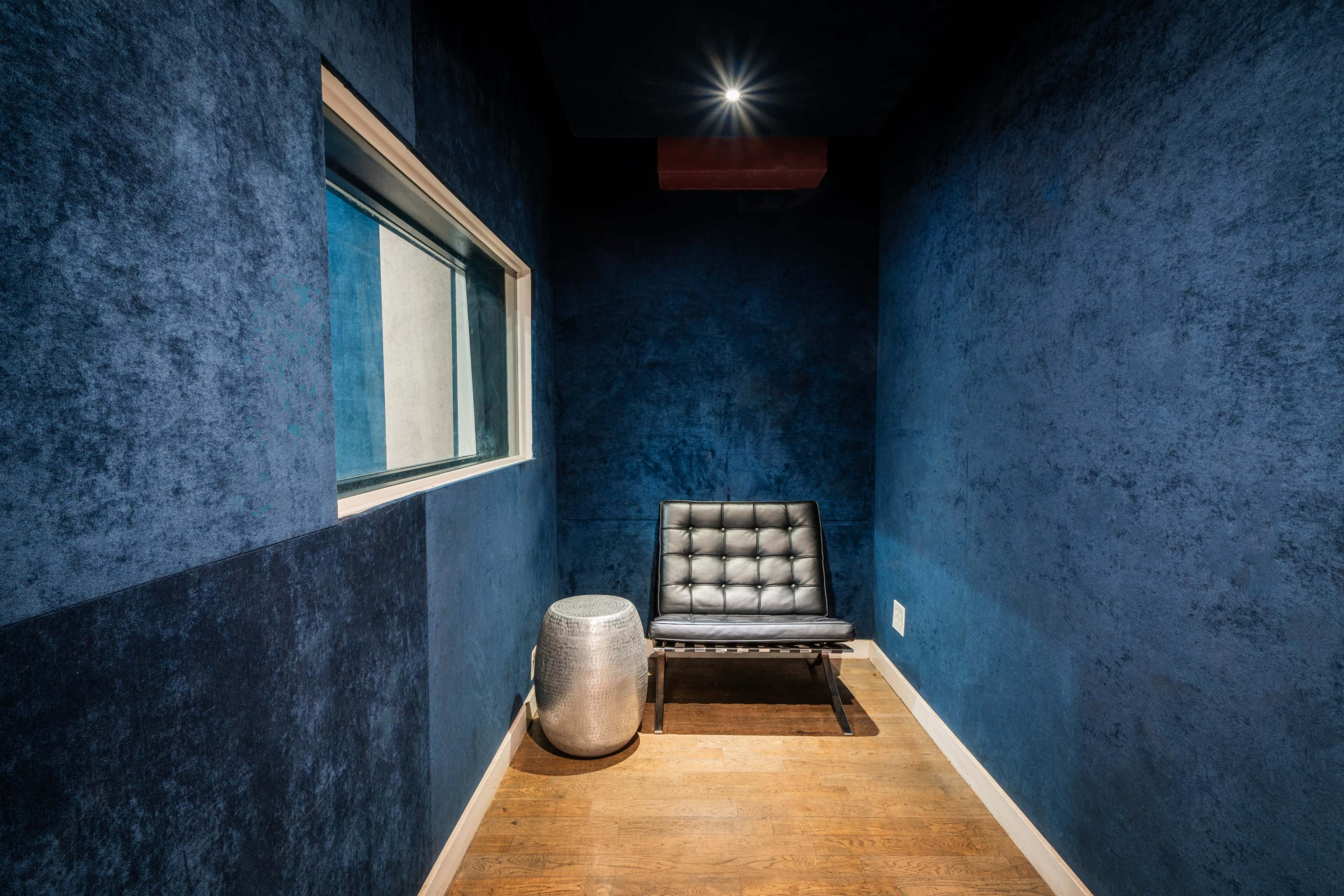 The image shows a small room with dark blue walls, featuring a black chair and a metallic accent table.