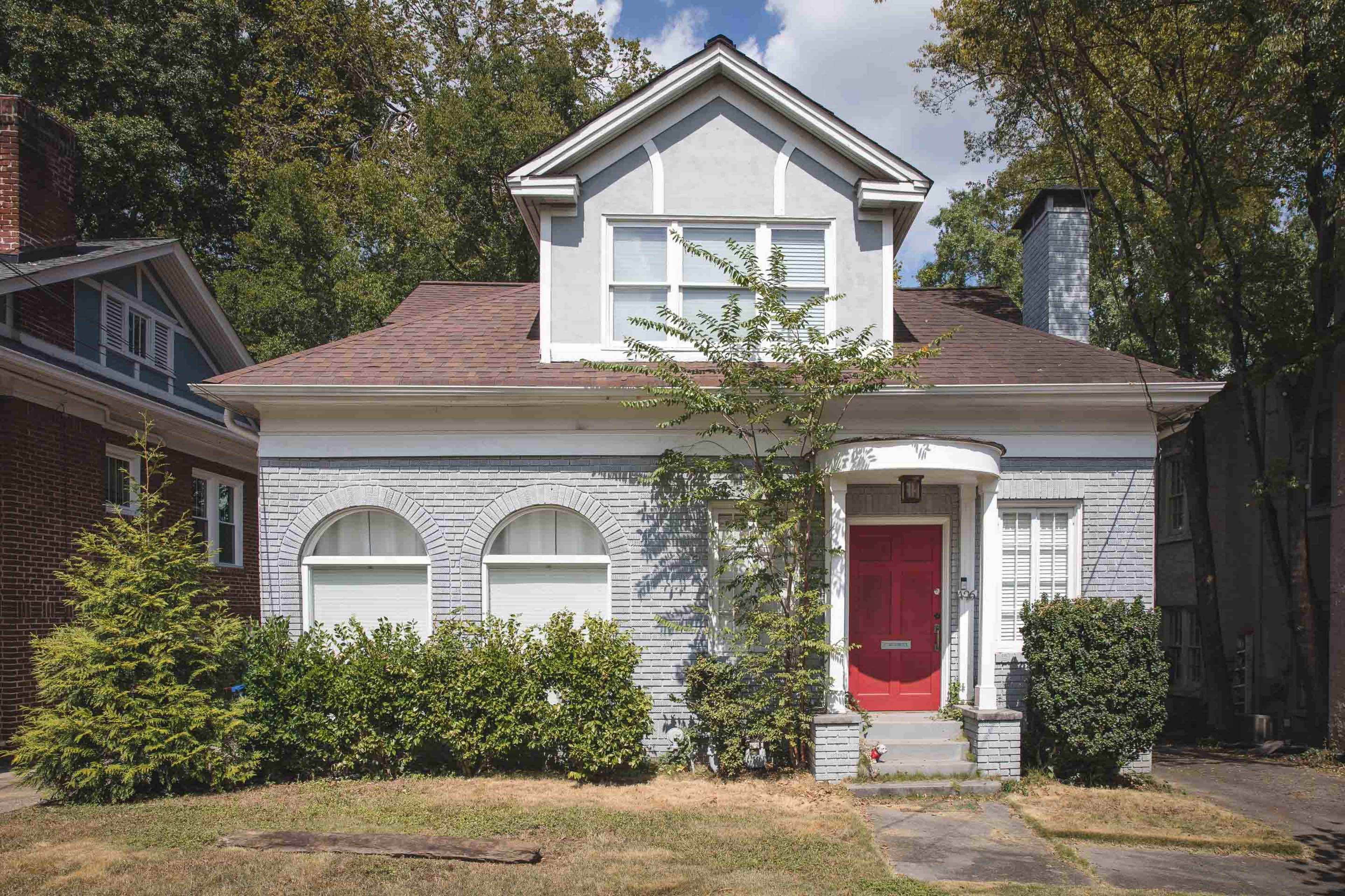 A gray house with a red door features arched windows and is surrounded by greenery.