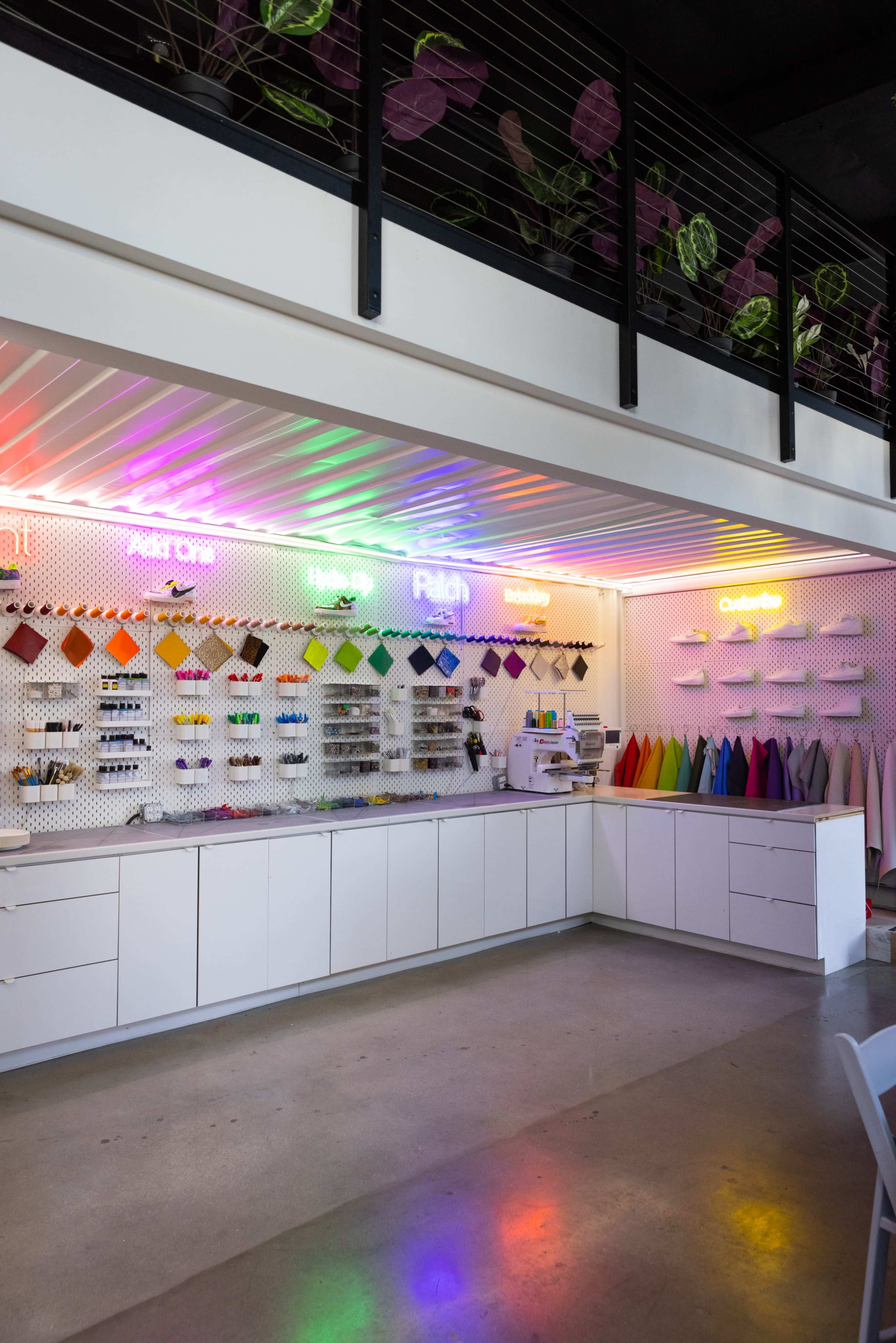 A colorful craft studio with a wall of organized craft materials and a sewing machine, illuminated by neon signs in vibrant colors.
