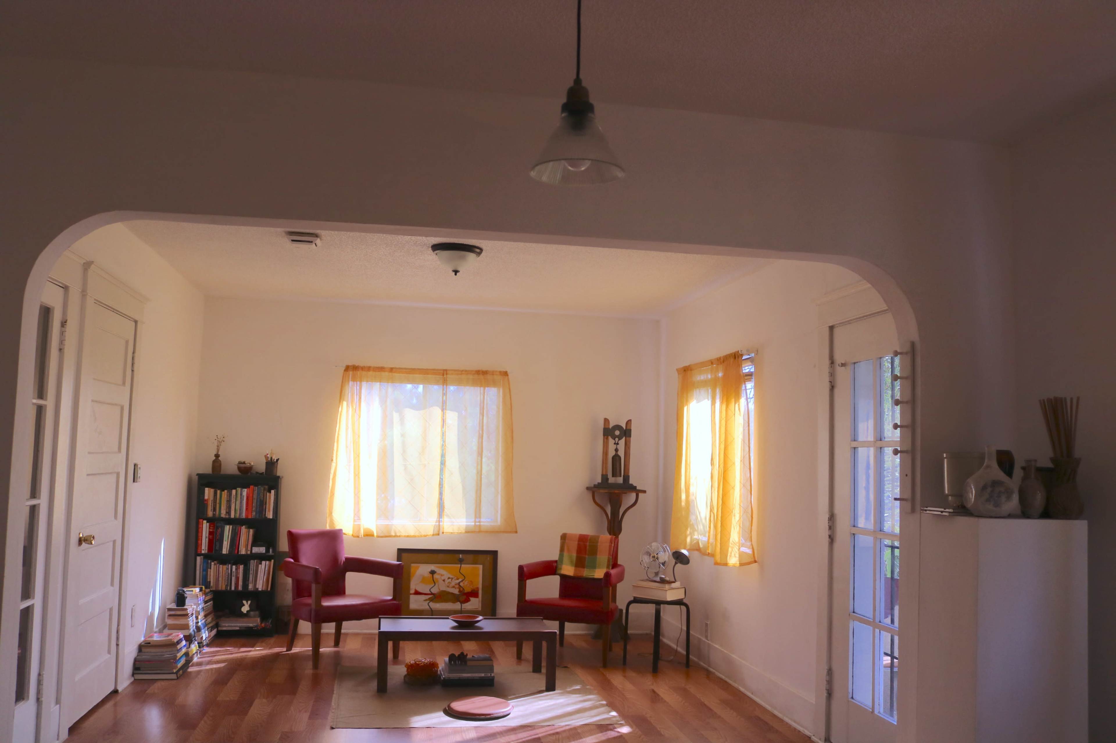 A brightly lit living room with two red chairs, a coffee table, and a window adorned with yellow curtains.