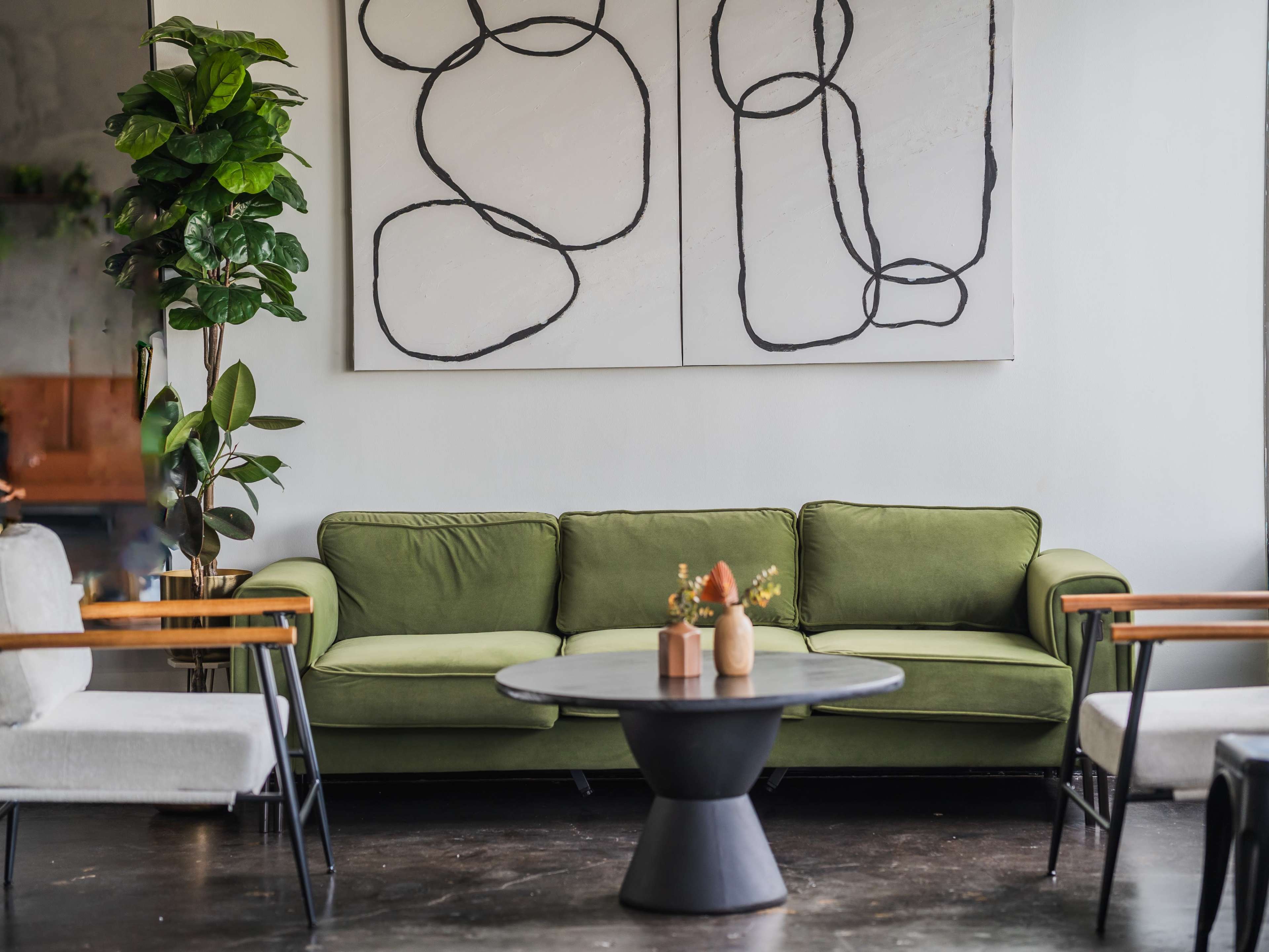 A green sofa sits in a modern room, accompanied by a round black coffee table and framed abstract wall art.
