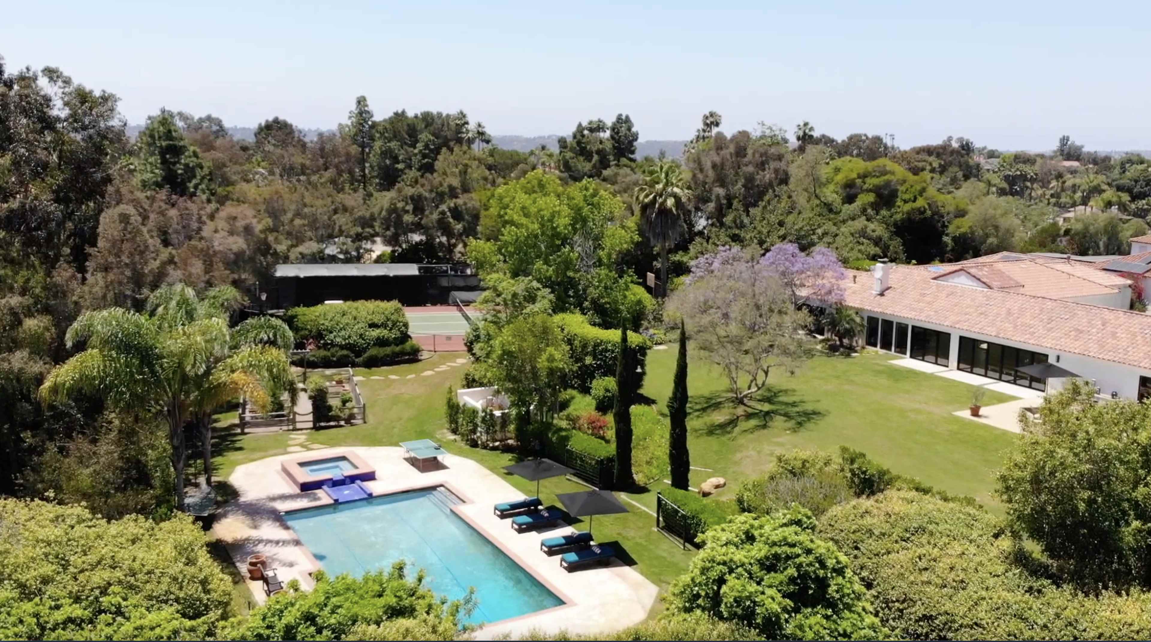 A spacious property featuring a swimming pool, landscaped gardens, and a modern house surrounded by trees.
