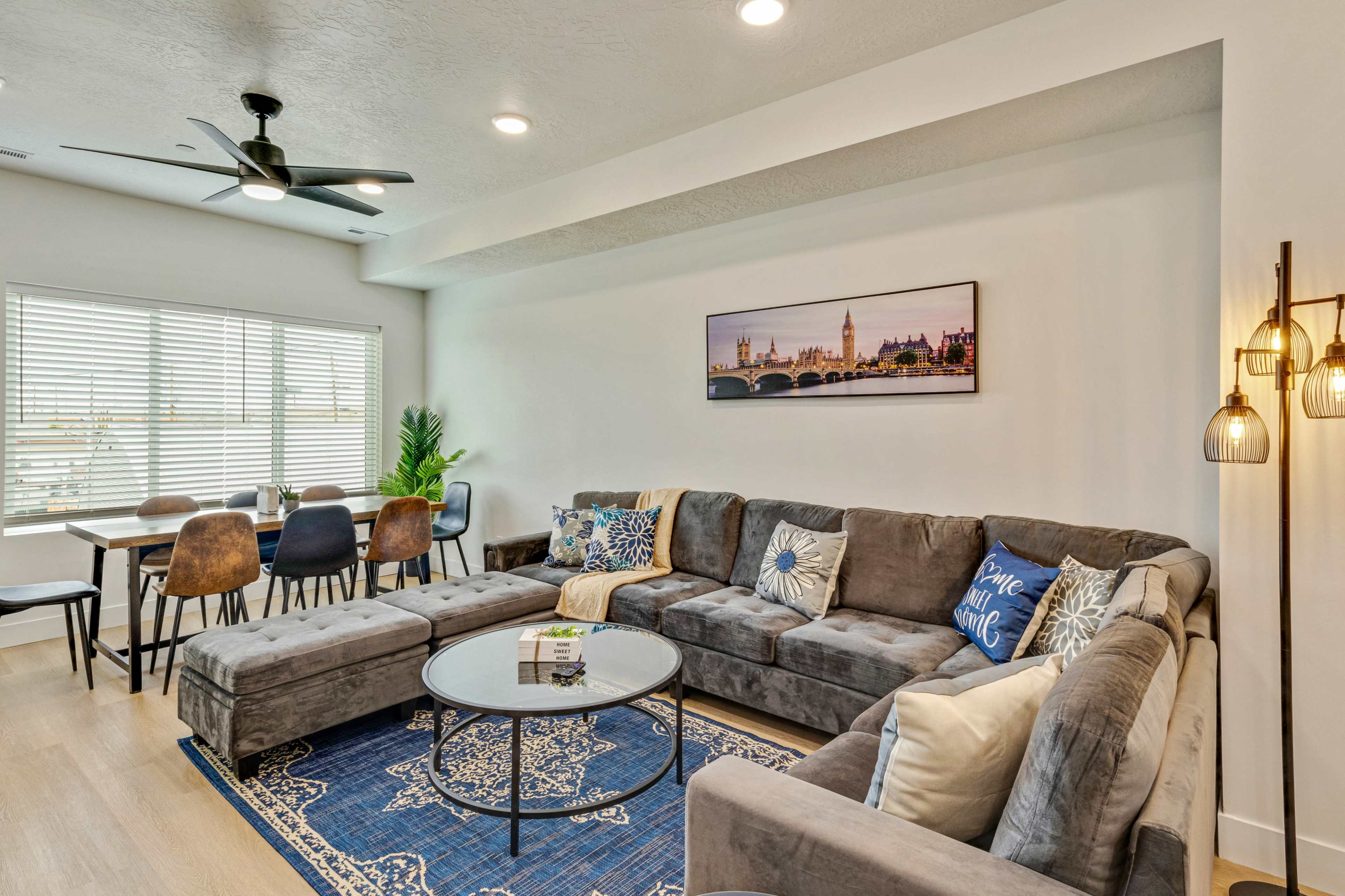 A modern living room with a sectional sofa, a round coffee table, and a dining area in the background featuring a table and chairs.