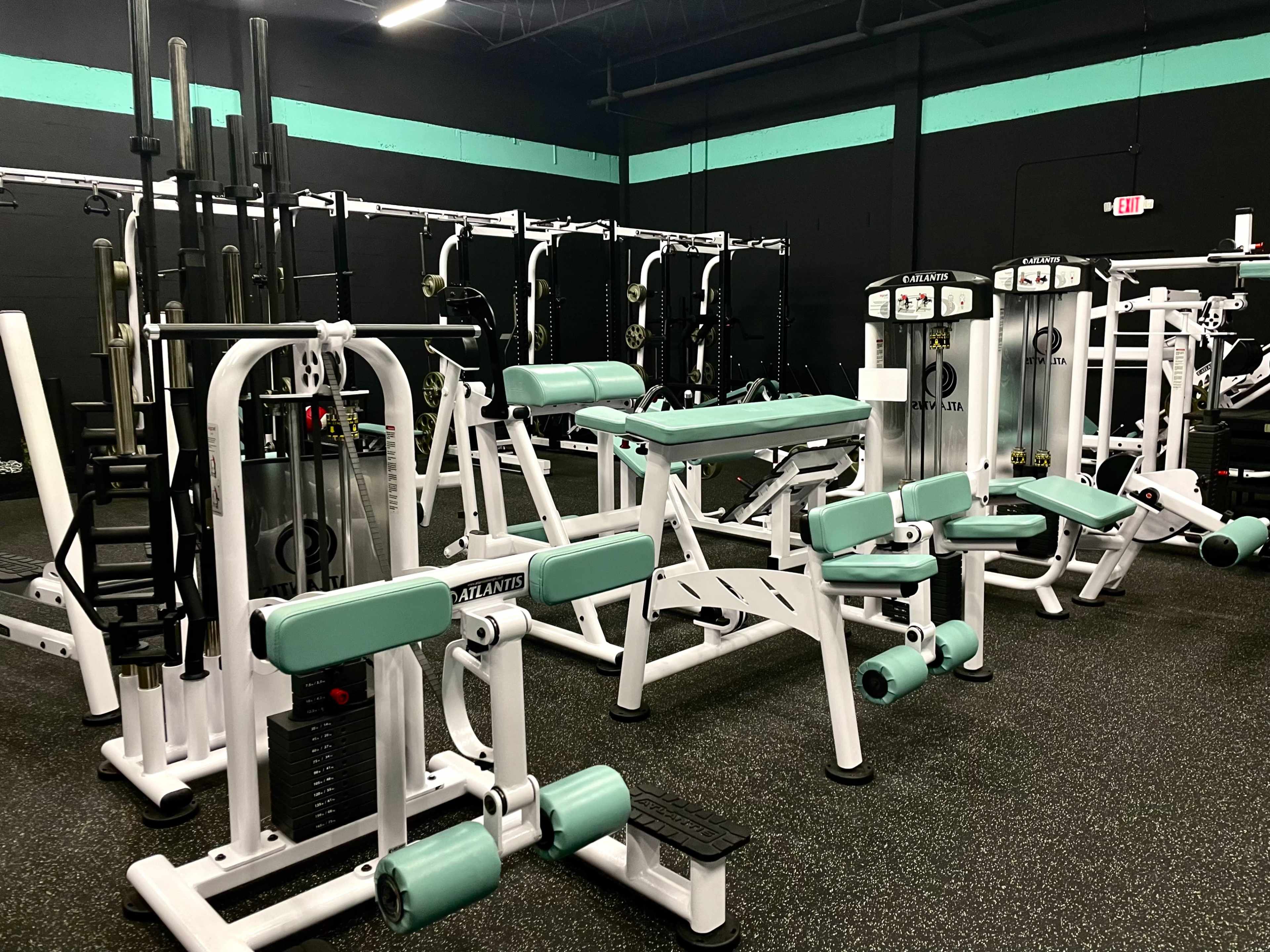 A gym interior equipped with various weightlifting machines and free weights arranged on a black rubber floor.